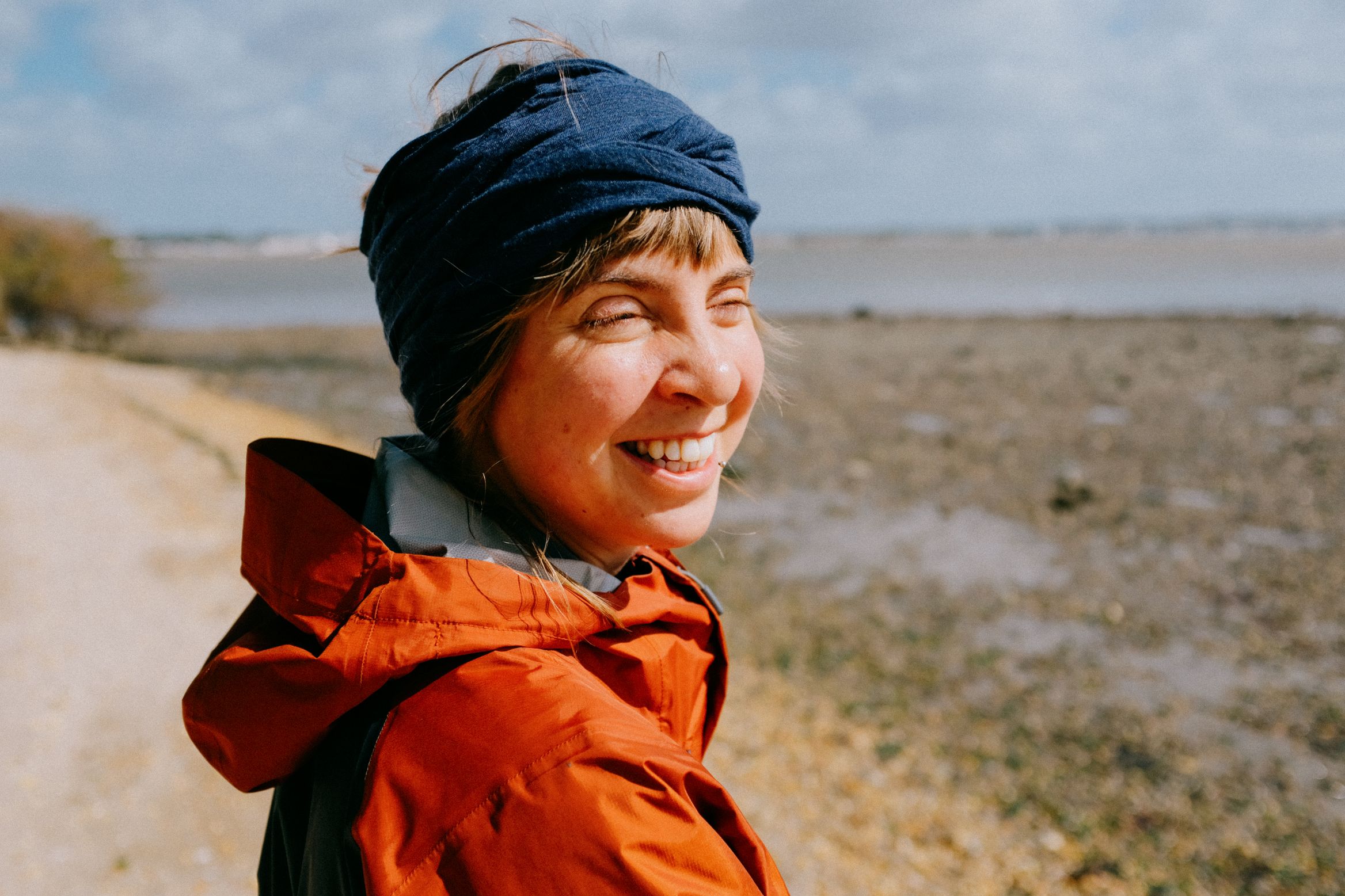 Grinning into the wind on the shore path, orange jacket, navy headband