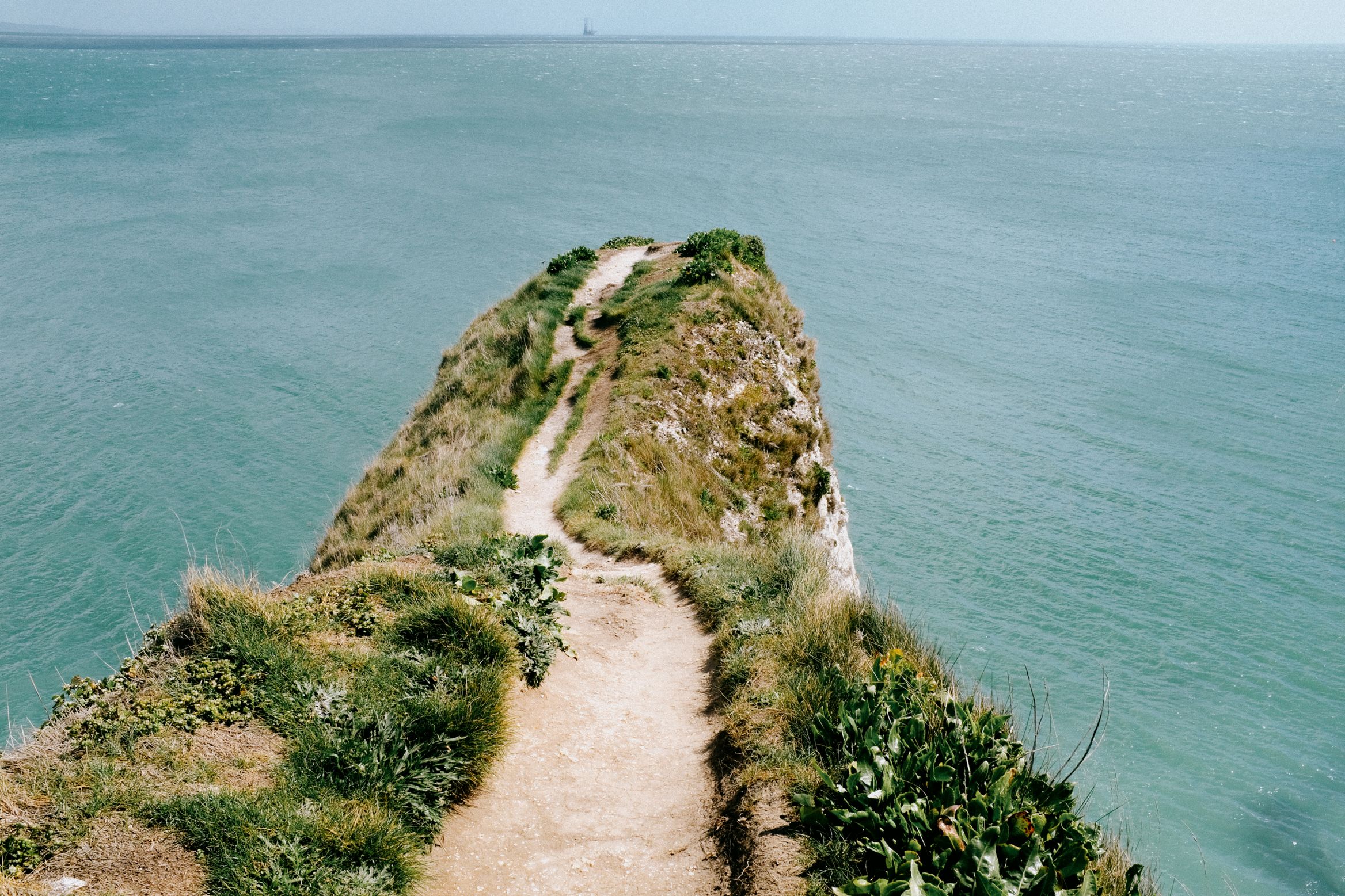 A footpath running out along a narrow headland into green water