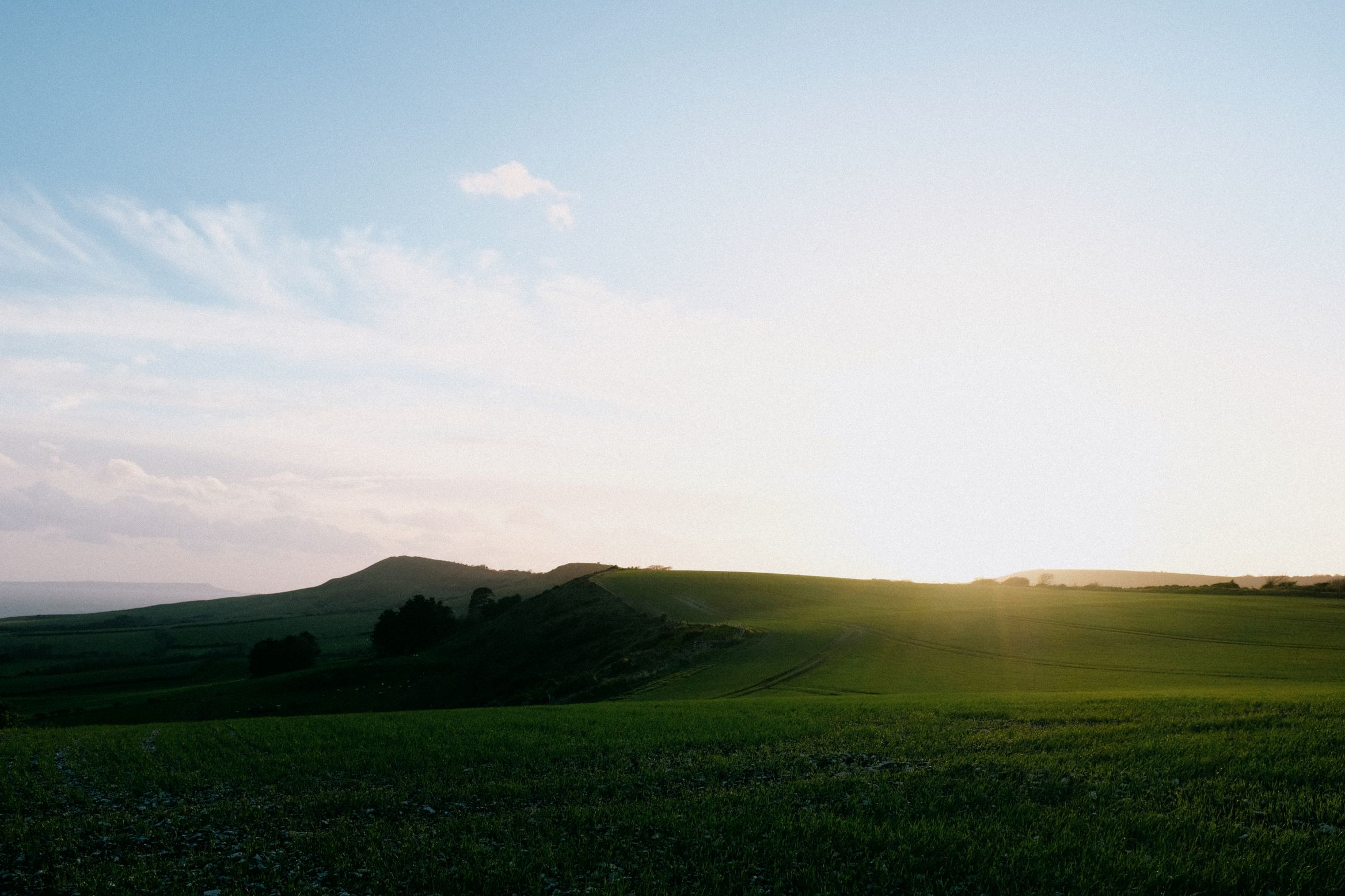 Sun going down behind a low ridge over a green field