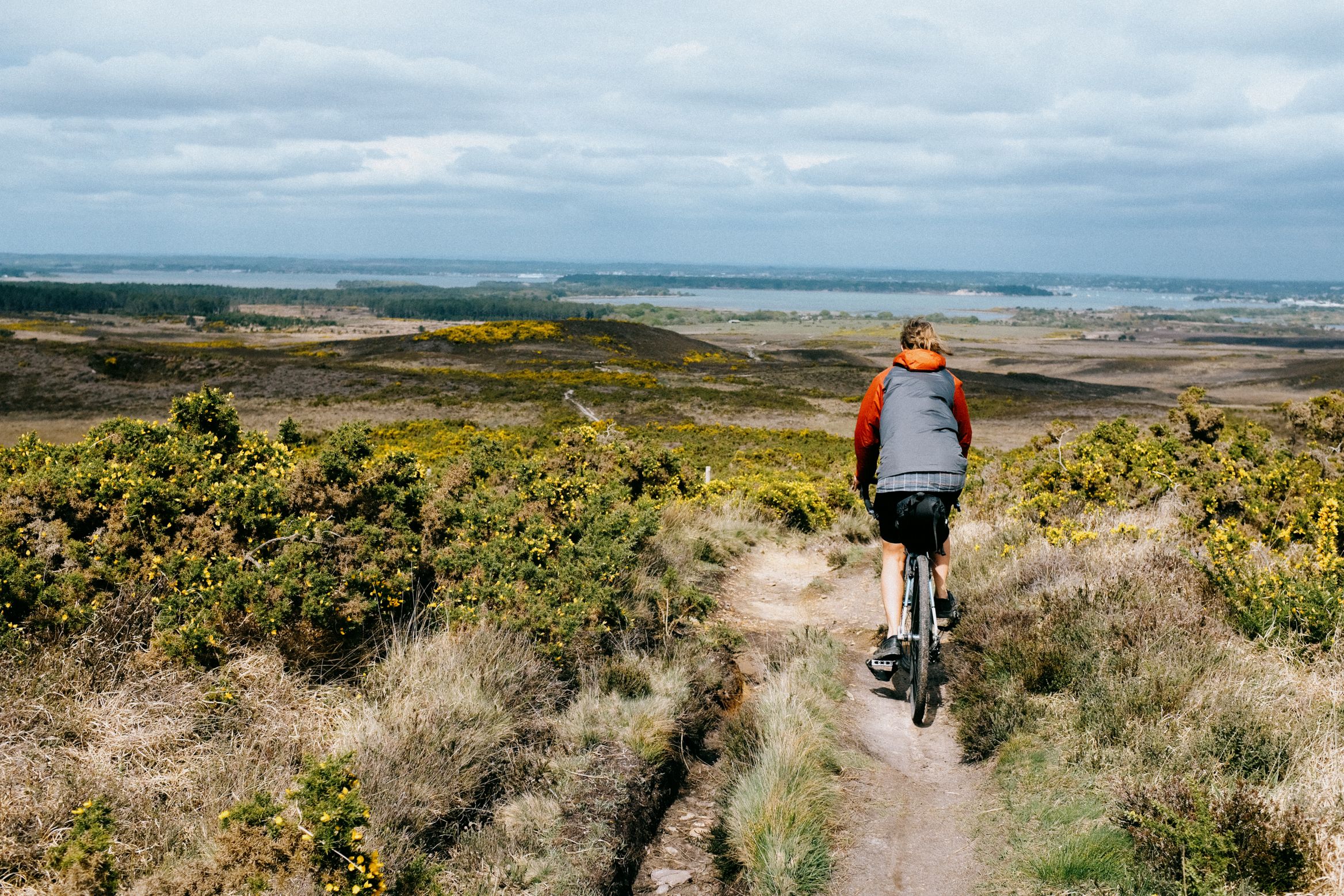 Dropping down a singletrack off the heath, water and low hills beyond