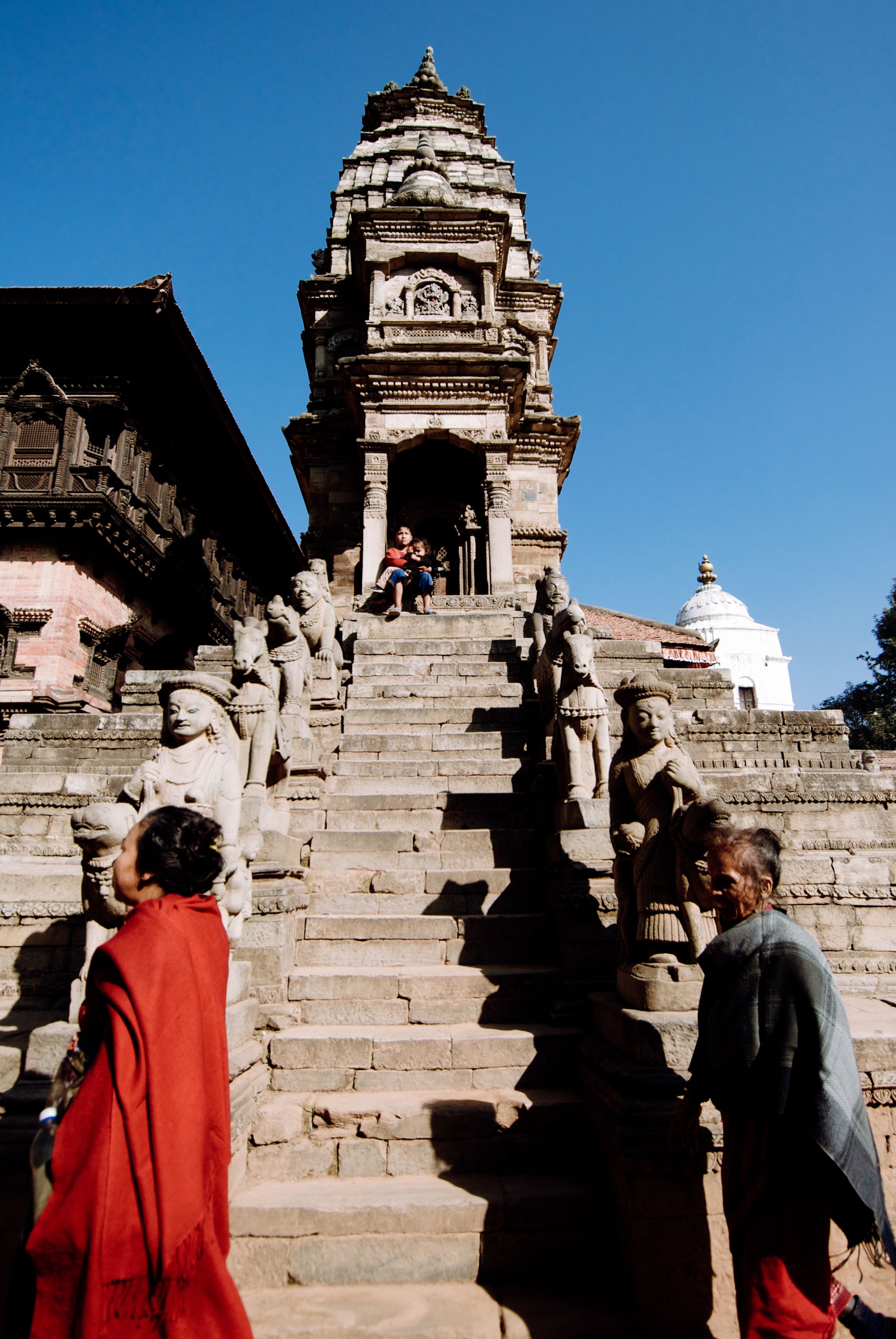 Steep temple steps flanked by pairs of stone guardians, people climbing past in red and grey