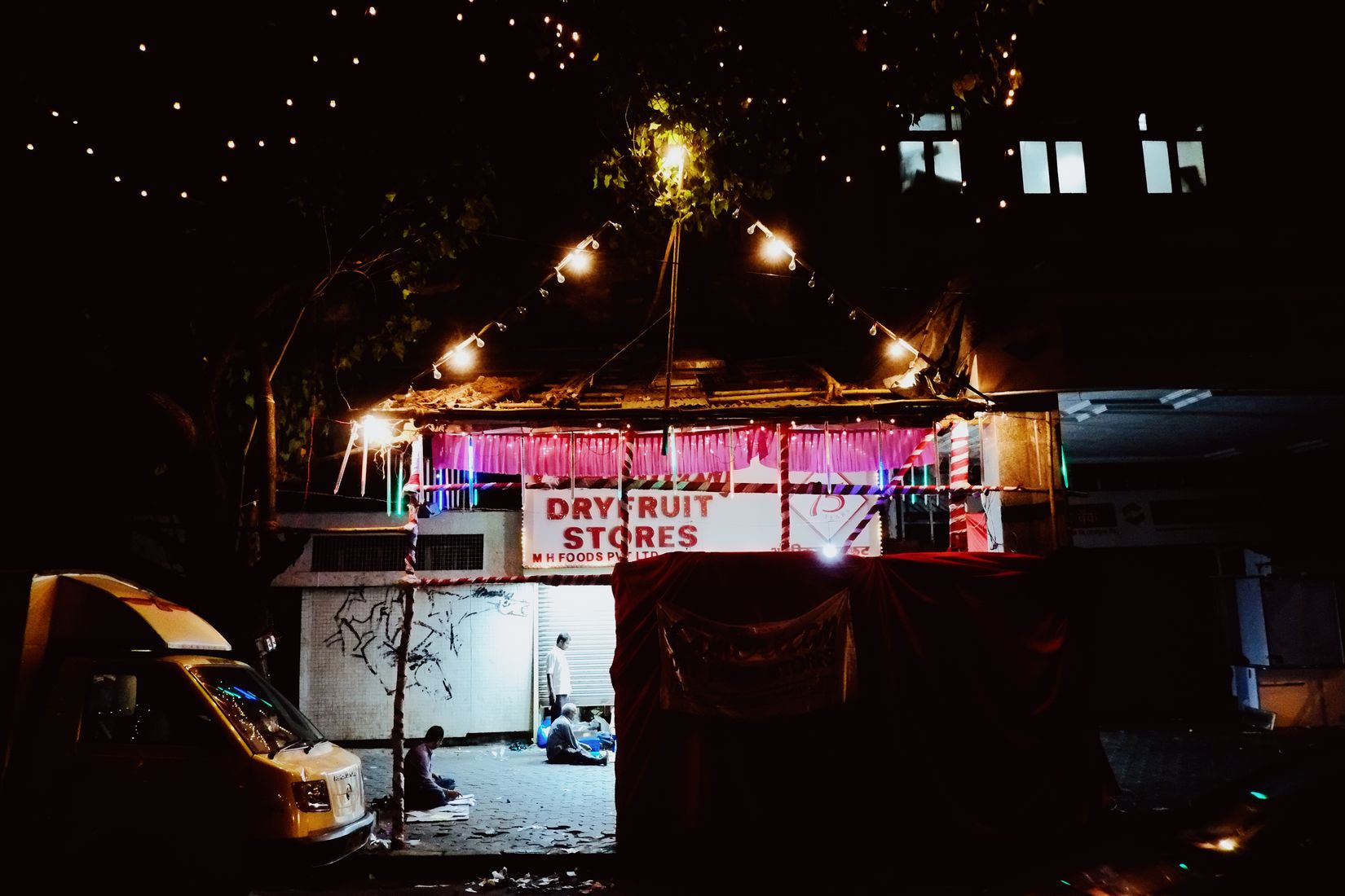 Closed fruit stand by night, with people sleeping outside.