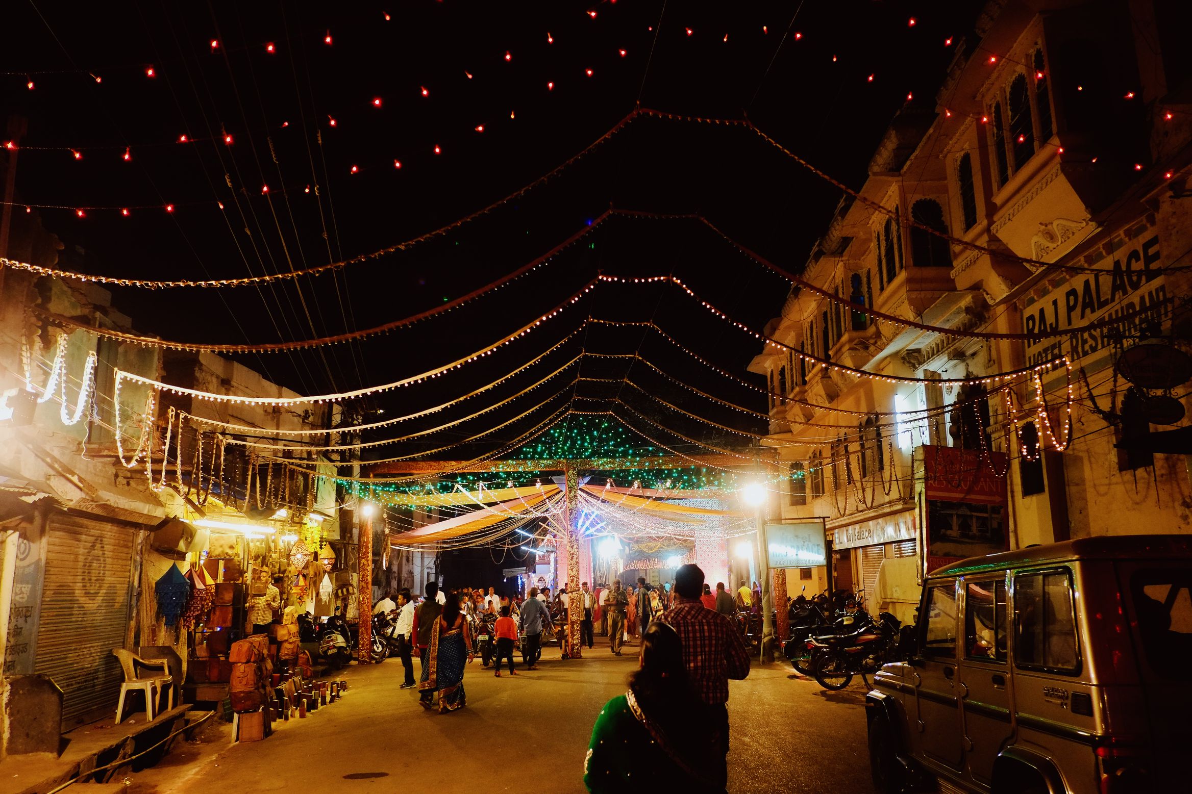 A wide street under converging lines of lights, a pandal tent glowing green at the far end