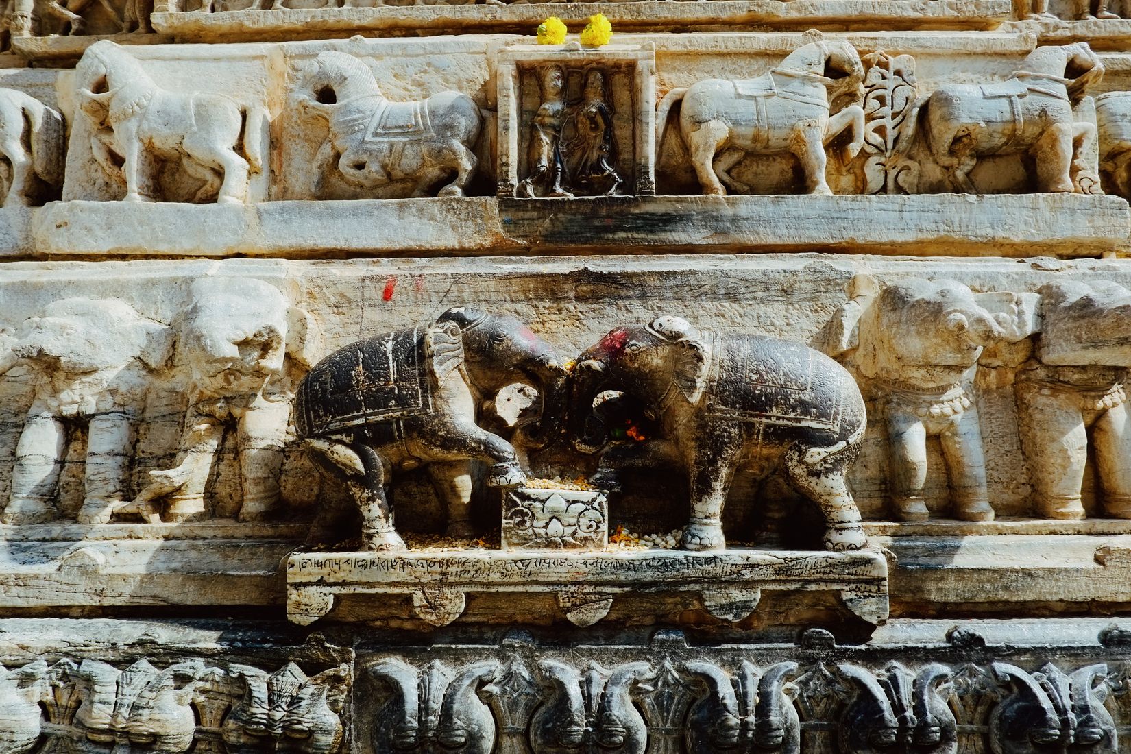 Two carved stone elephants facing each other on a temple frieze, worn smooth and marked with red powder