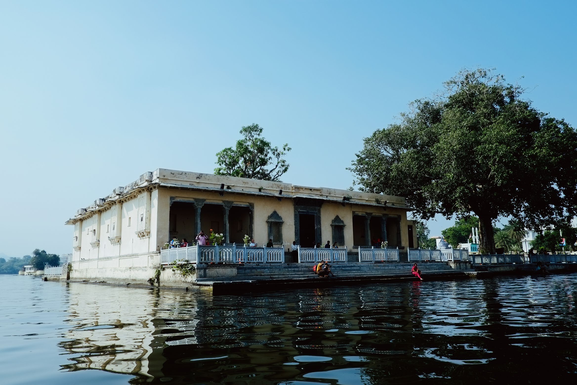 A low colonnaded building standing straight out of the lake, a tree leaning over its roof