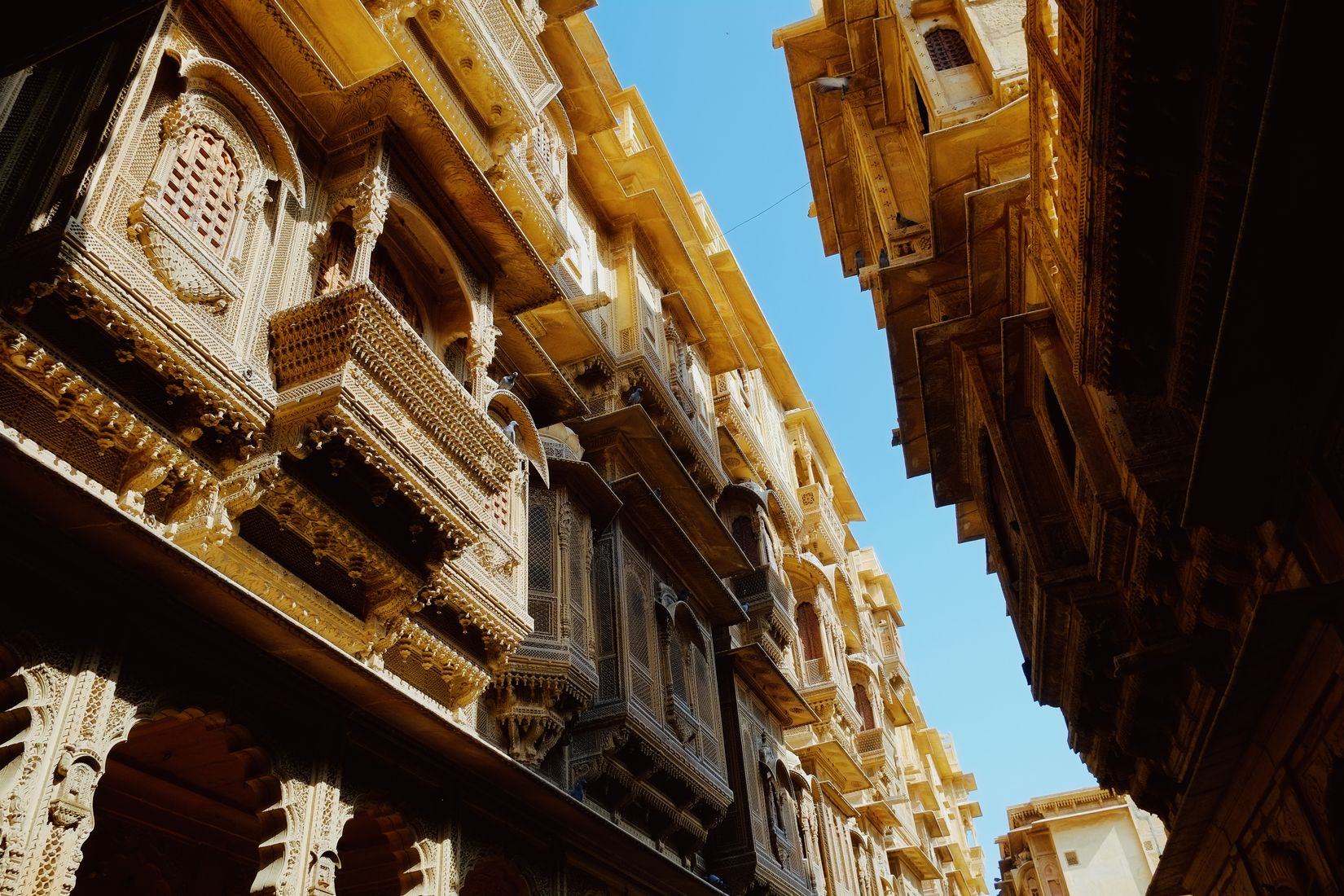Carved sandstone balconies stacked up both sides of a lane, meeting a narrow strip of blue sky