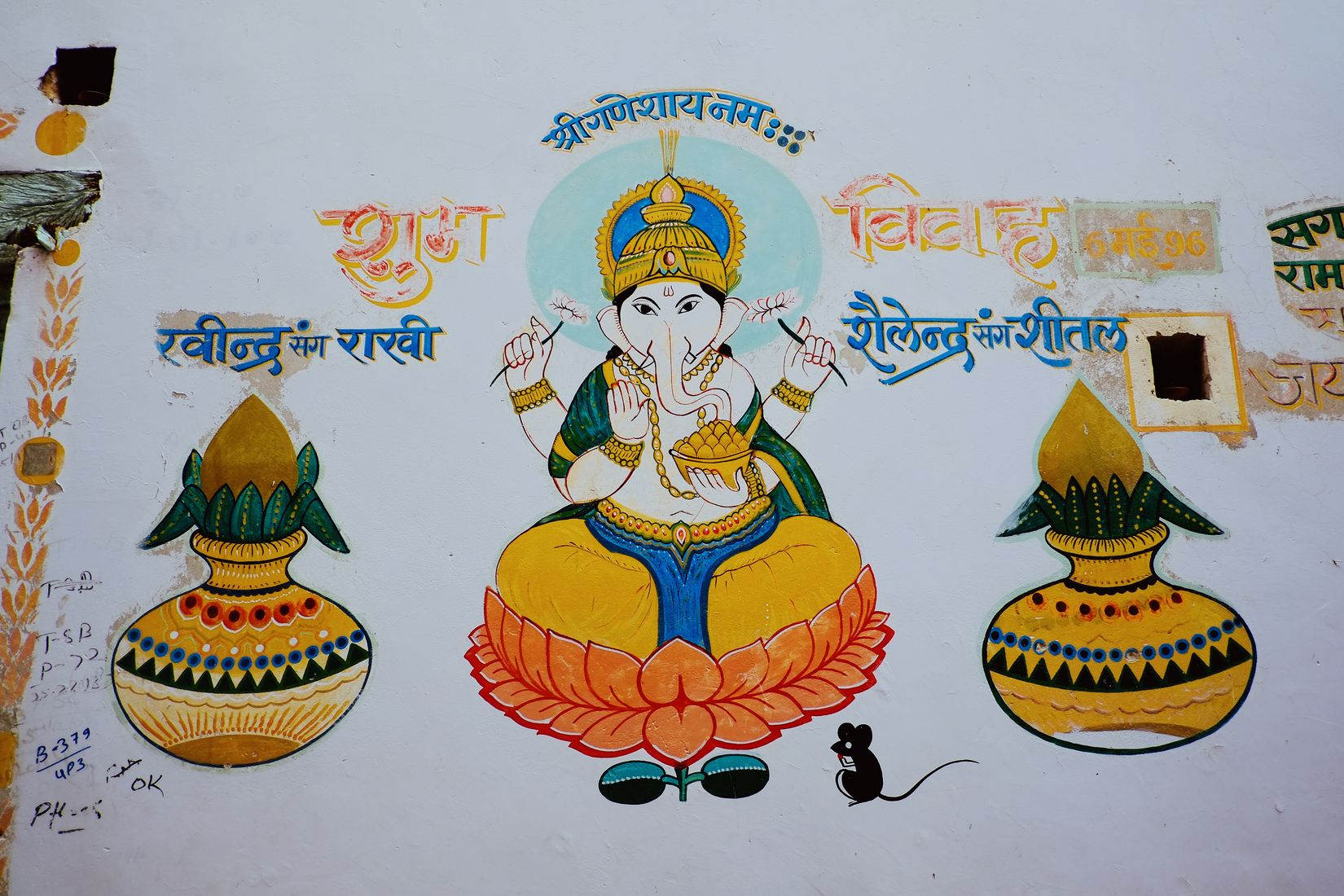 A wedding mural painted on a whitewashed wall — Ganesh on a lotus between two pots, a mouse at his feet