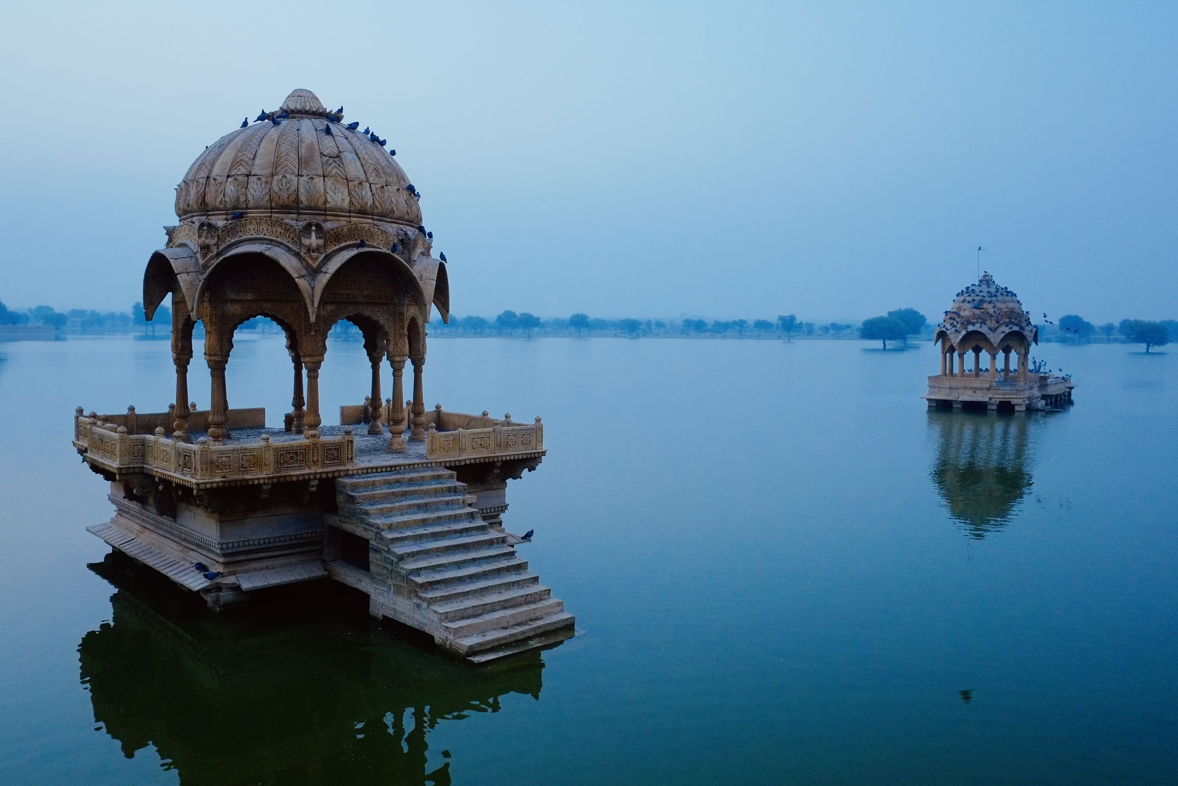 Two domed cenotaphs standing out in still water at dawn, pigeons crowded on the nearer roof