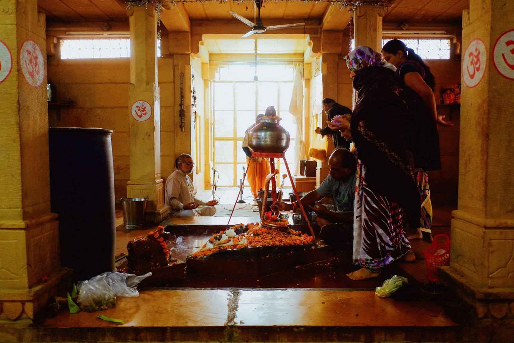 Inside a yellow stone temple, a brass pot raised on a stand over a bed of marigolds, women gathered at the side