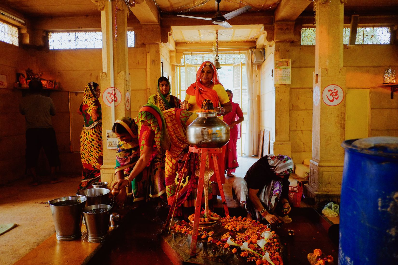 The same temple from the front, women in bright print saris filling steel buckets around the offering