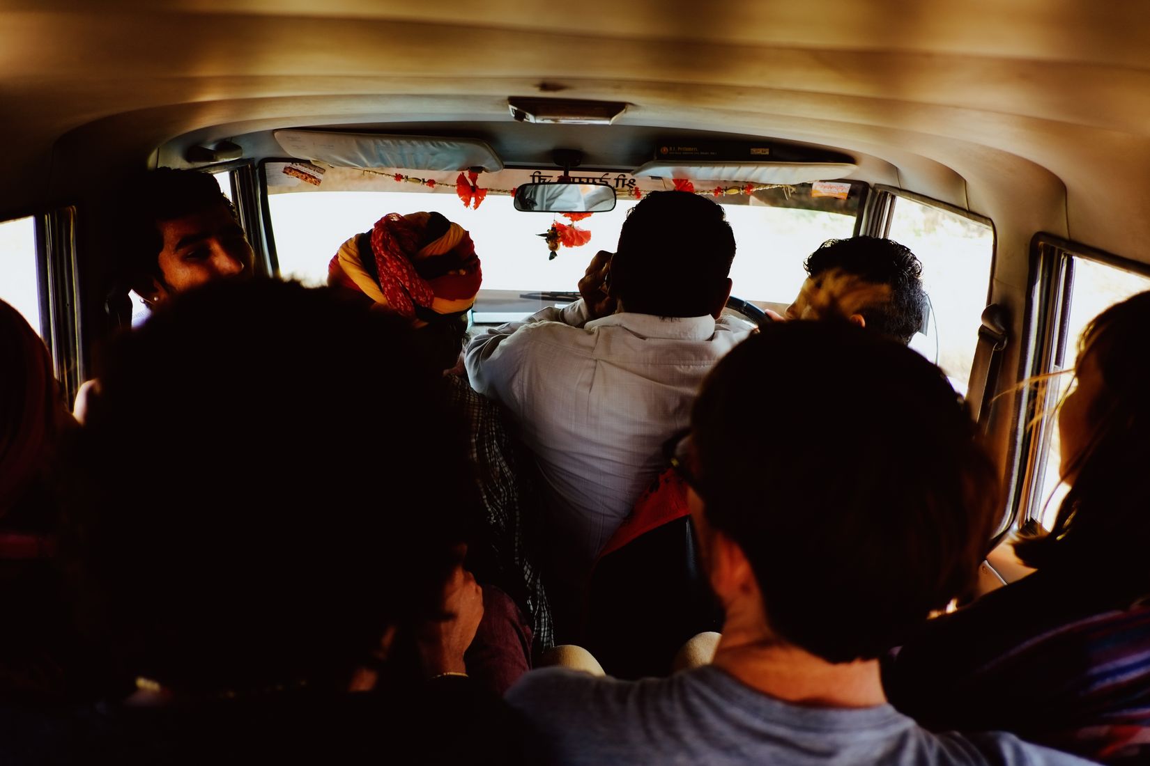 Packed into the back of a shared jeep, heads and shoulders filling the frame, the road bright through the windscreen