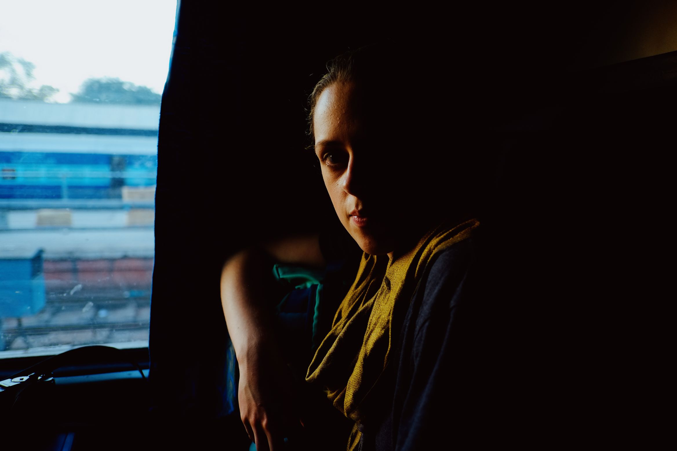 Amy on the train, half in shadow against the window, a platform sliding past behind her