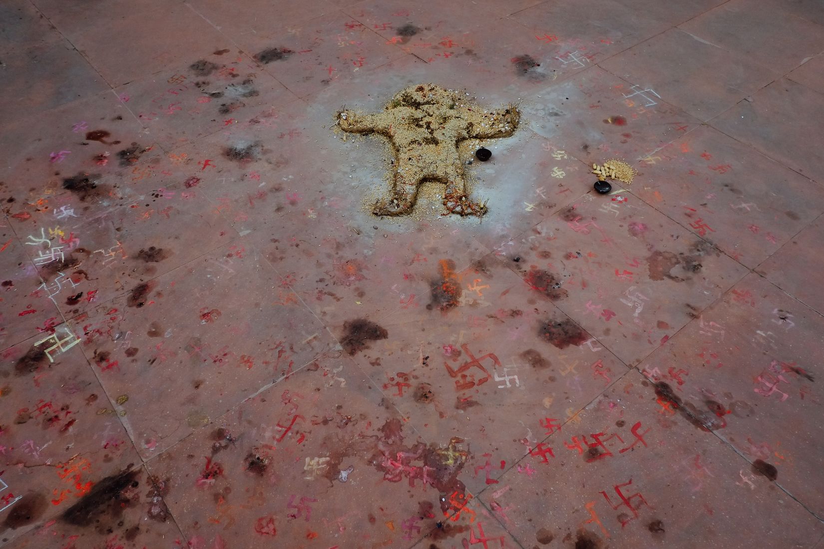 A stone floor covered in chalk and pigment marks around a small moulded figure, left from a ritual