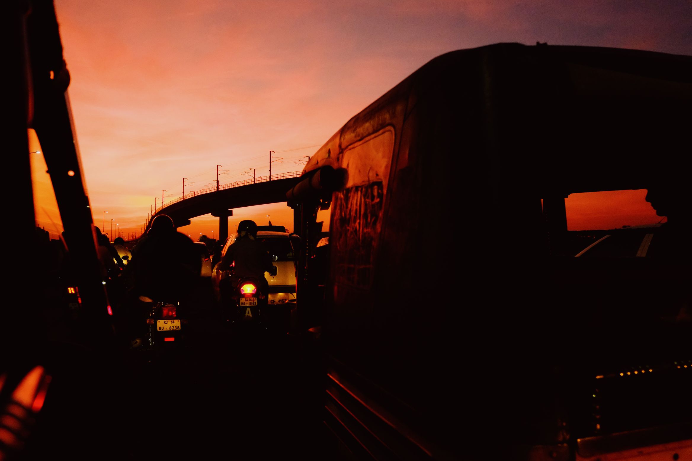 Stuck in traffic at sunset, a bus and motorbikes in silhouette against an orange sky under a flyover