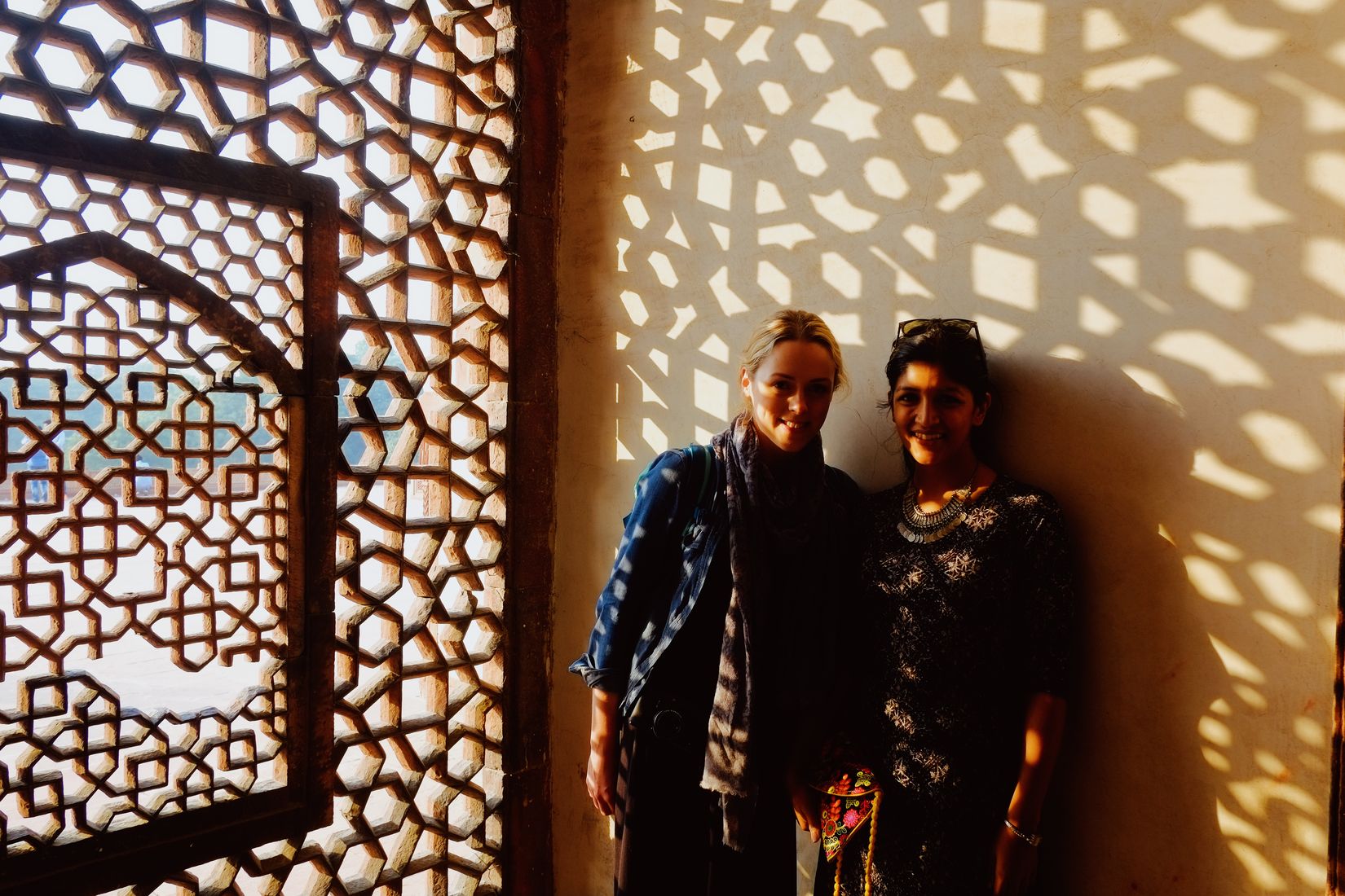 Amy and a woman she got talking to, standing against a wall thrown all over with the lattice shadow of the screen