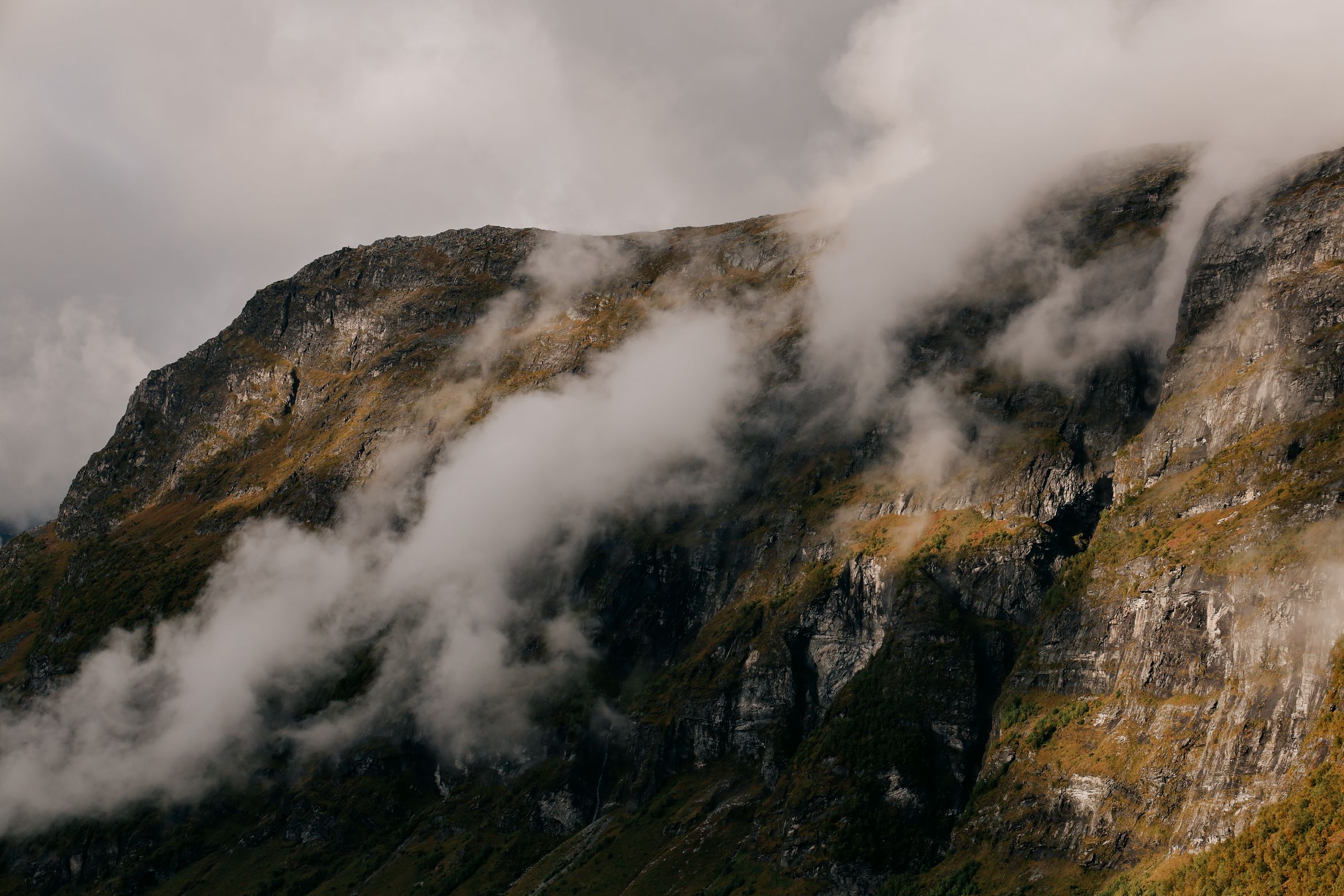 Clouds tearing across a steep green and grey mountainside