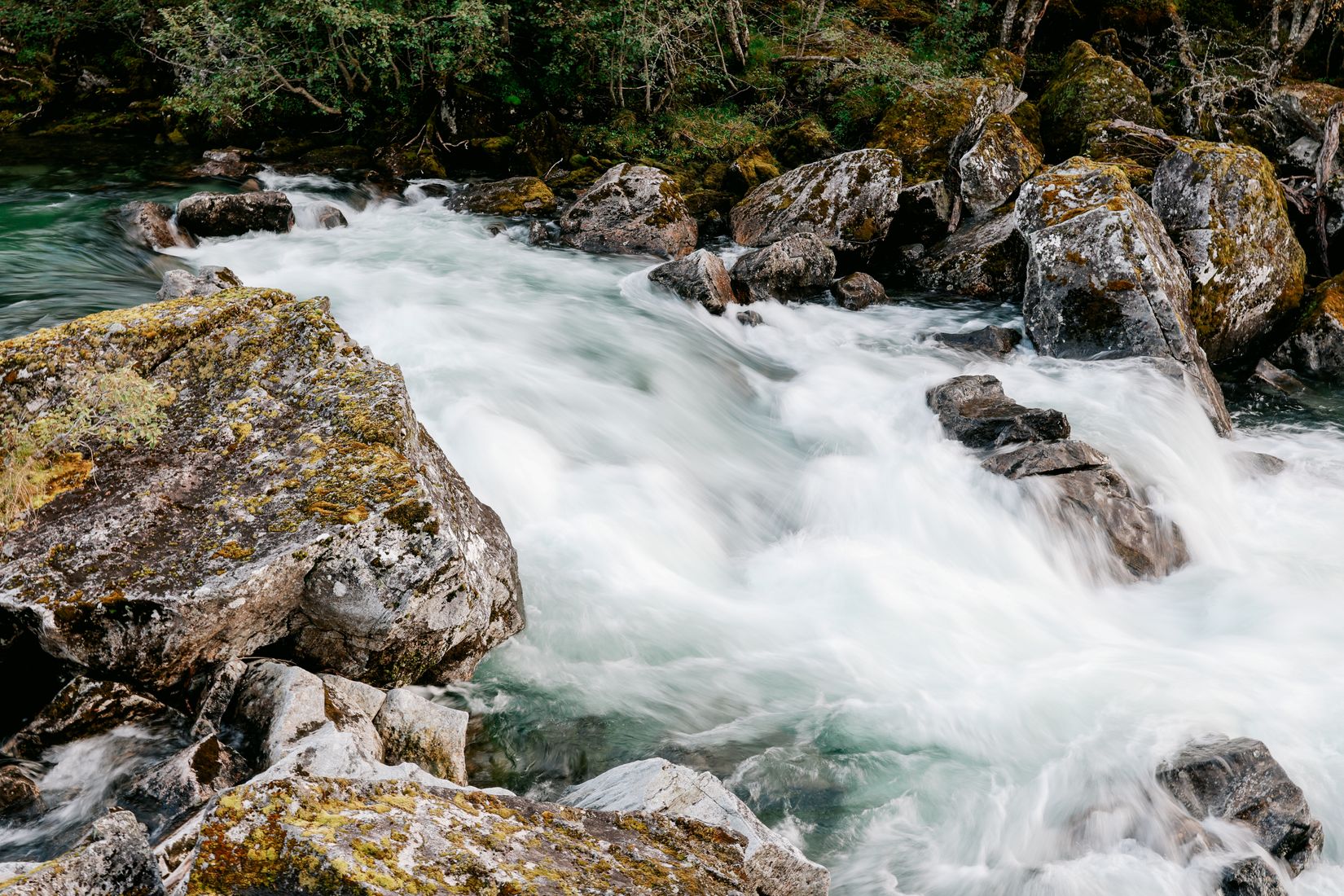 Long exposure of white water rushing between lichen-covered boulders