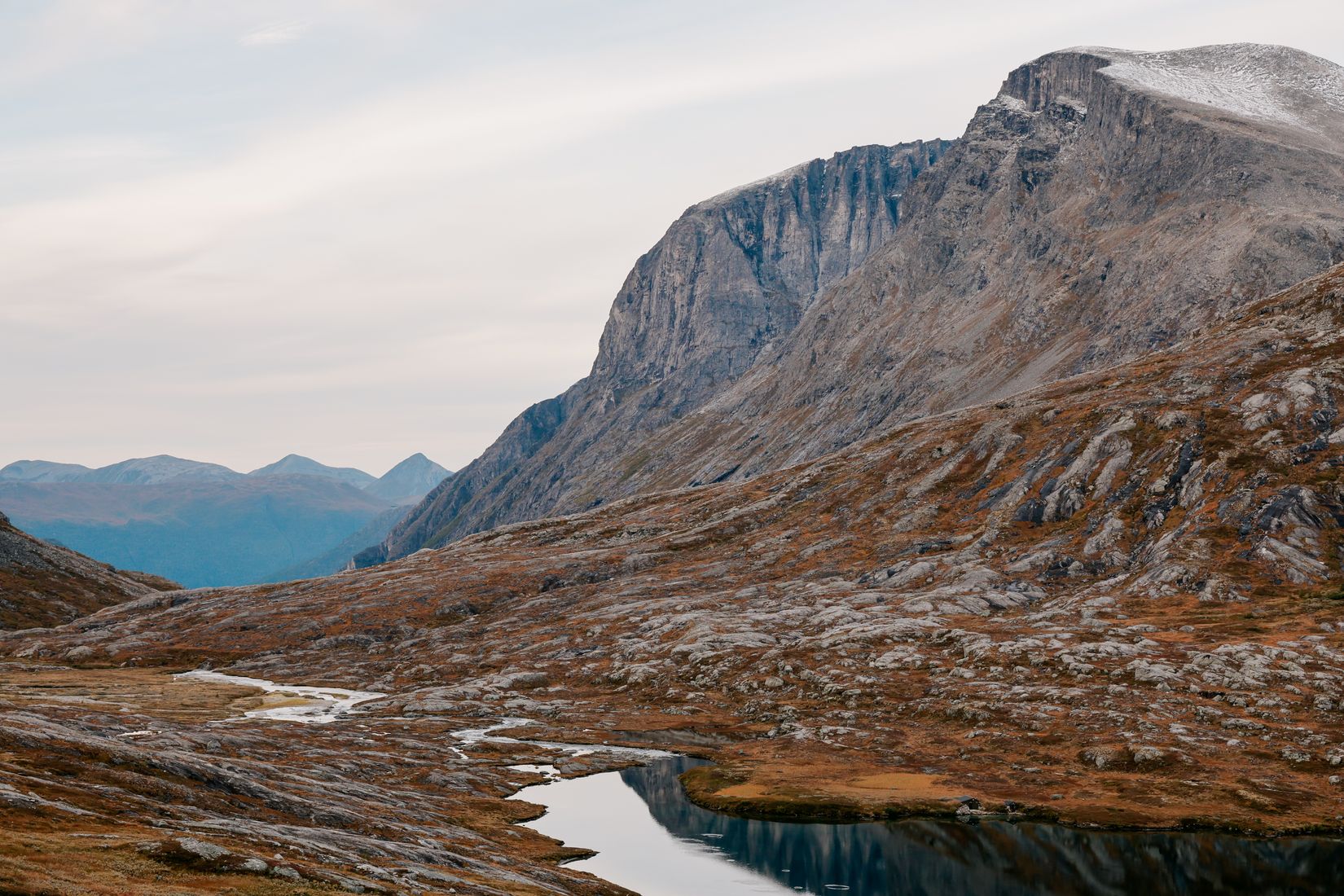 Bare grey crags above the pass, a thread of water running through rust-coloured heath below