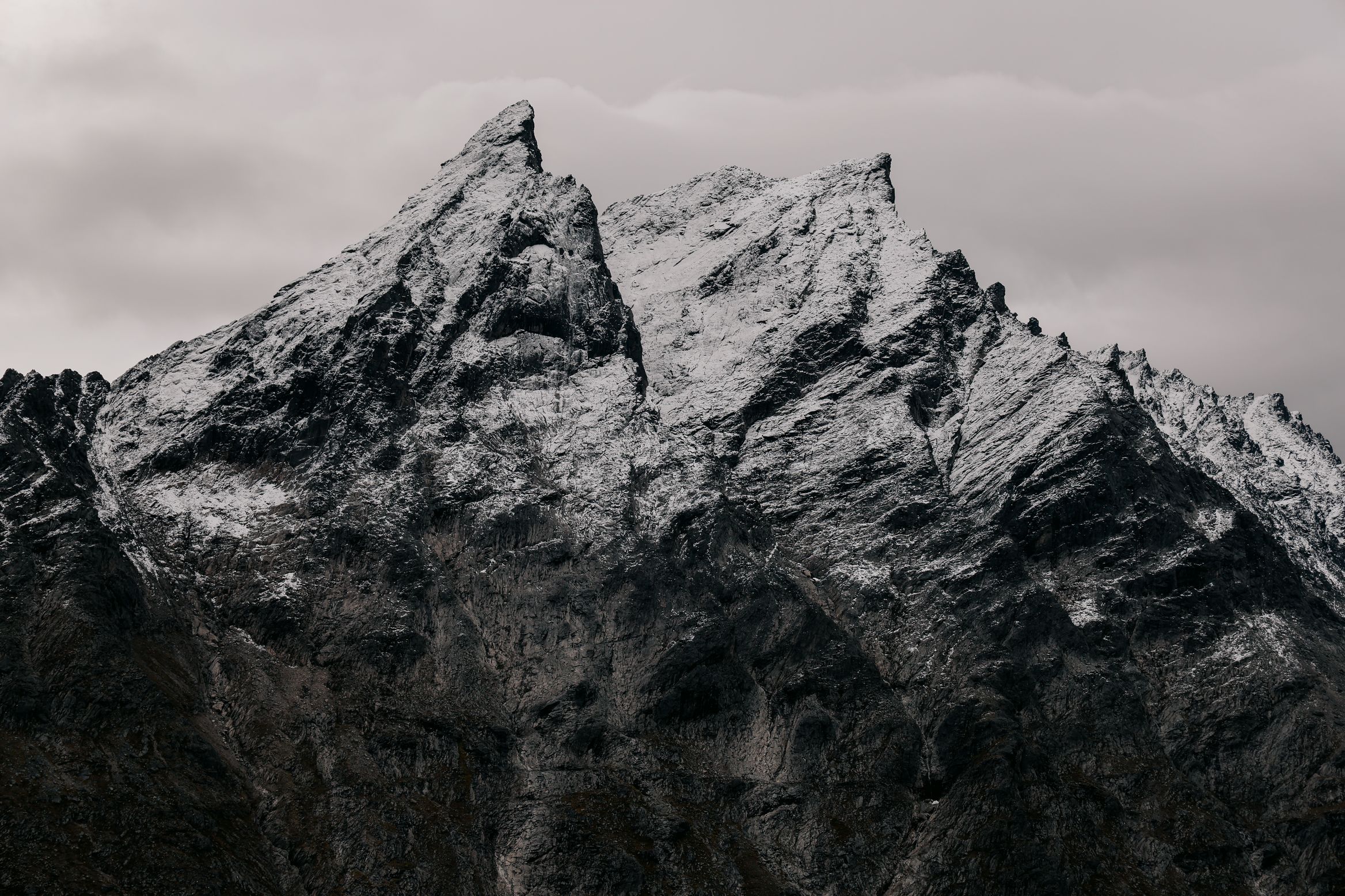 Black and white: fresh snow on the jagged ridge of a mountain under flat cloud