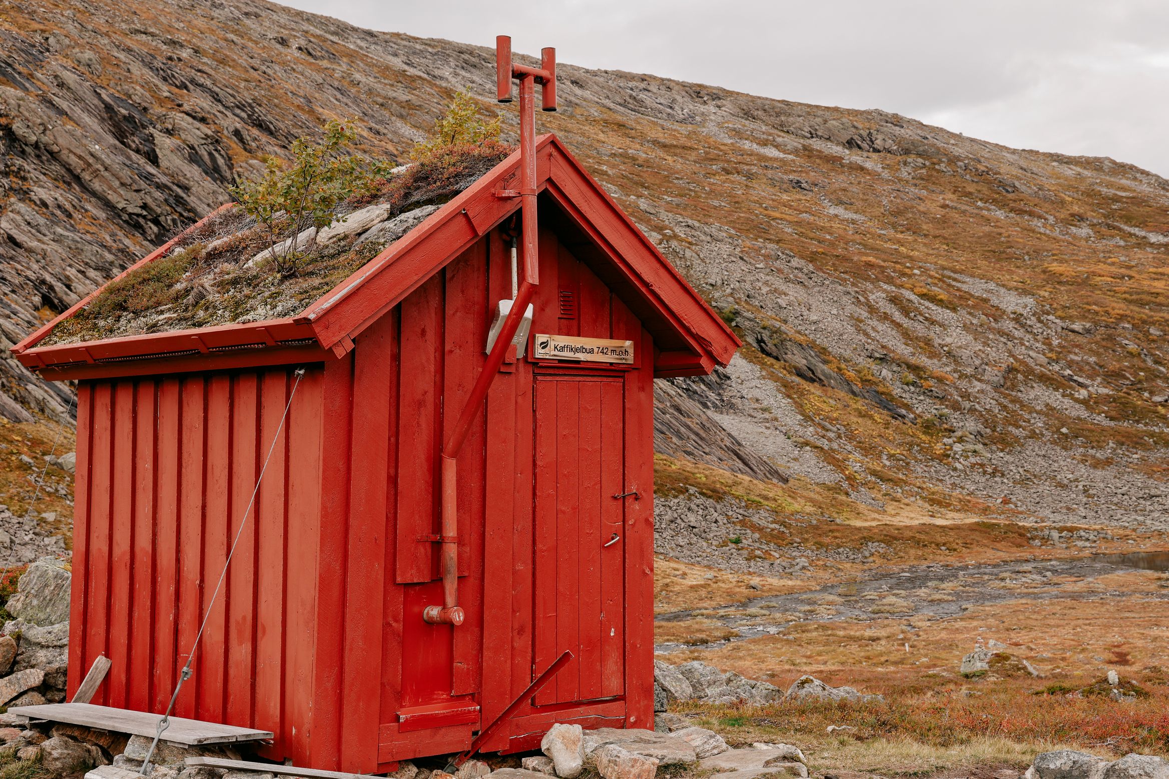 A small red turf-roofed hut with a signboard by its door, propped against the wind on a bare hillside