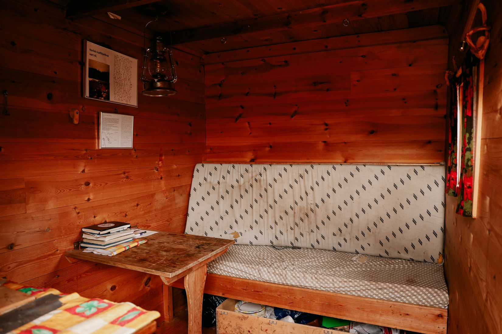 Inside the hut: a paraffin lamp, a bench with a striped cushion, and a table stacked with books