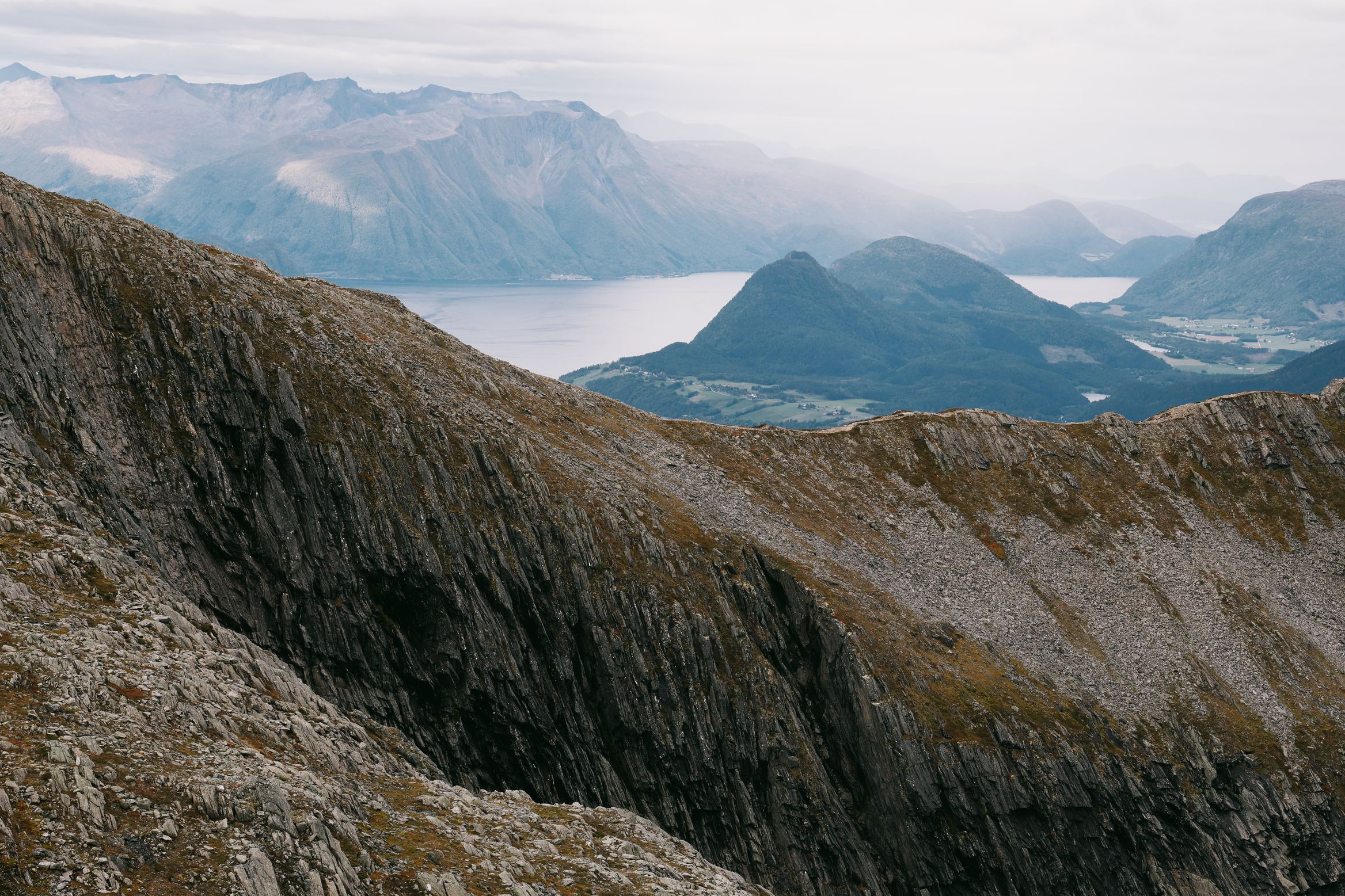 A knife-edge ridge dropping away to a hazy fjord and layered blue hills beyond