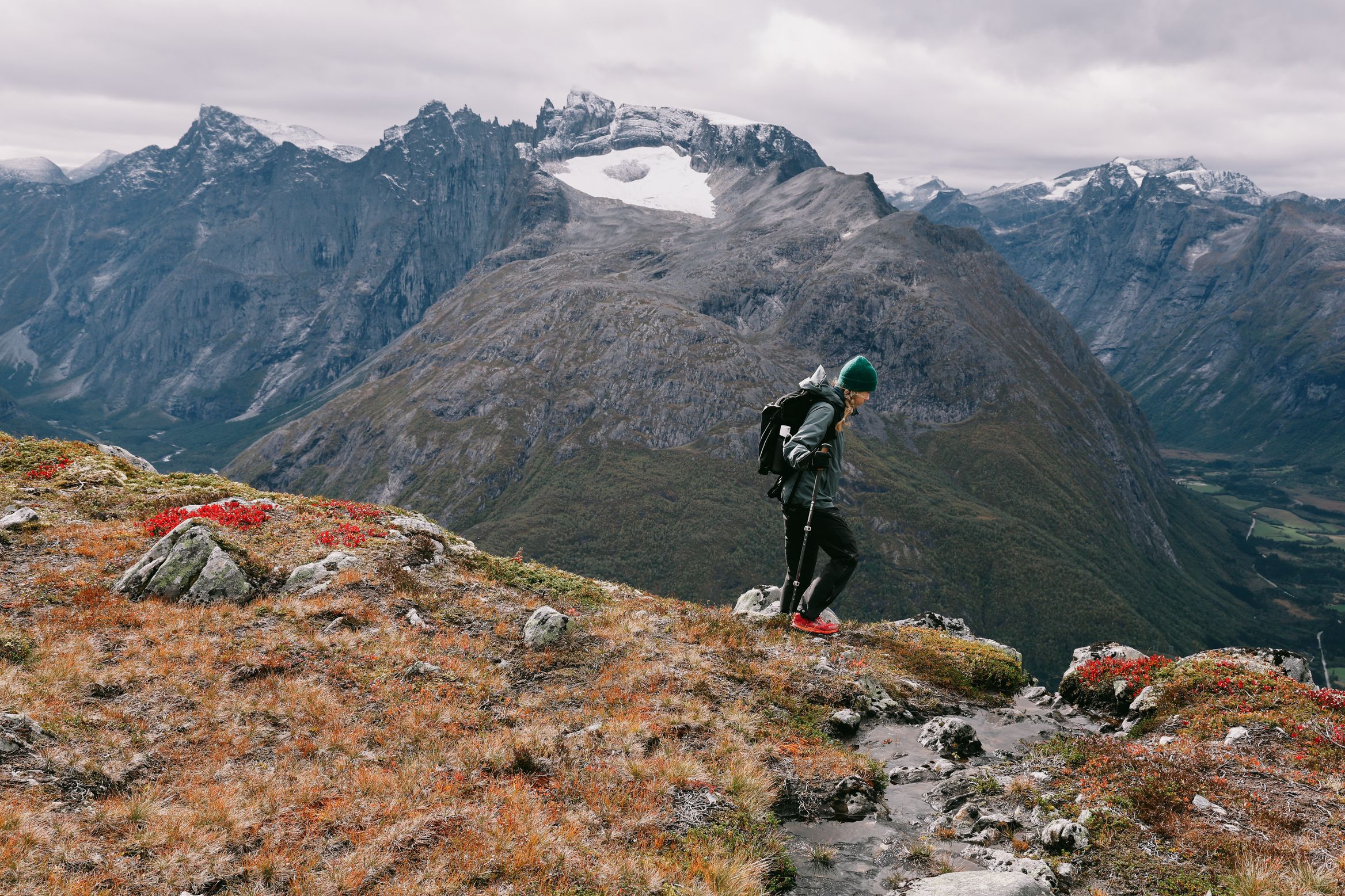 A walker on the skyline of Romsdalseggen, a glacier-capped massif filling the valley behind