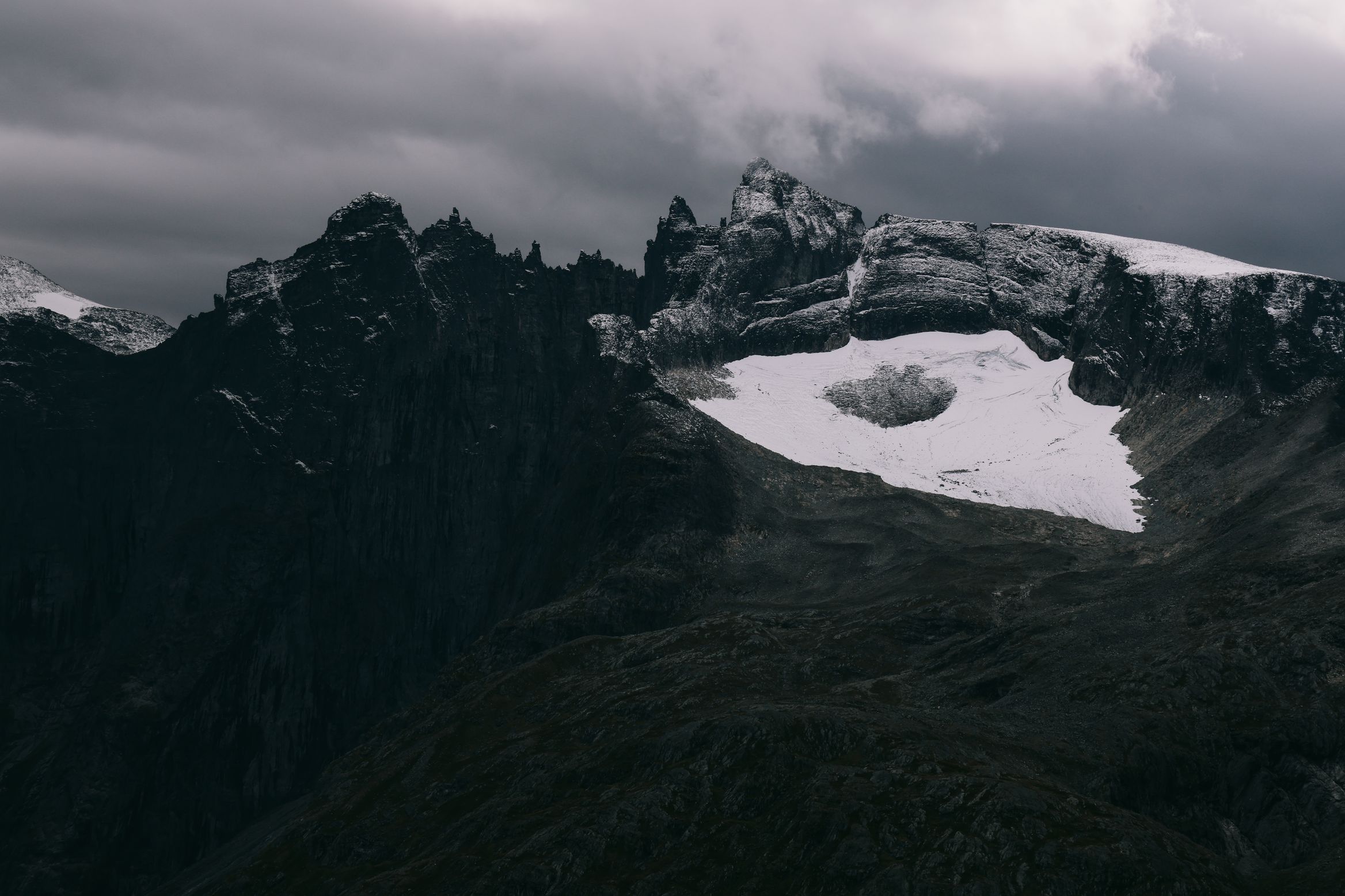 A hanging snowfield caught in a dark rock bowl under broken cloud