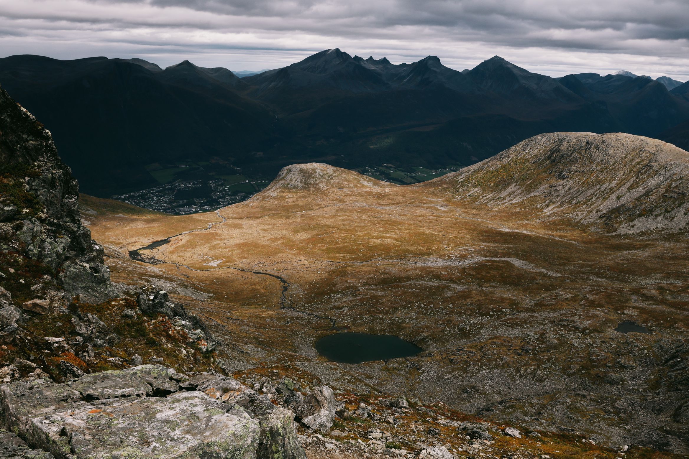 A small dark tarn in a bowl of golden moorland, a wall of peaks on the horizon