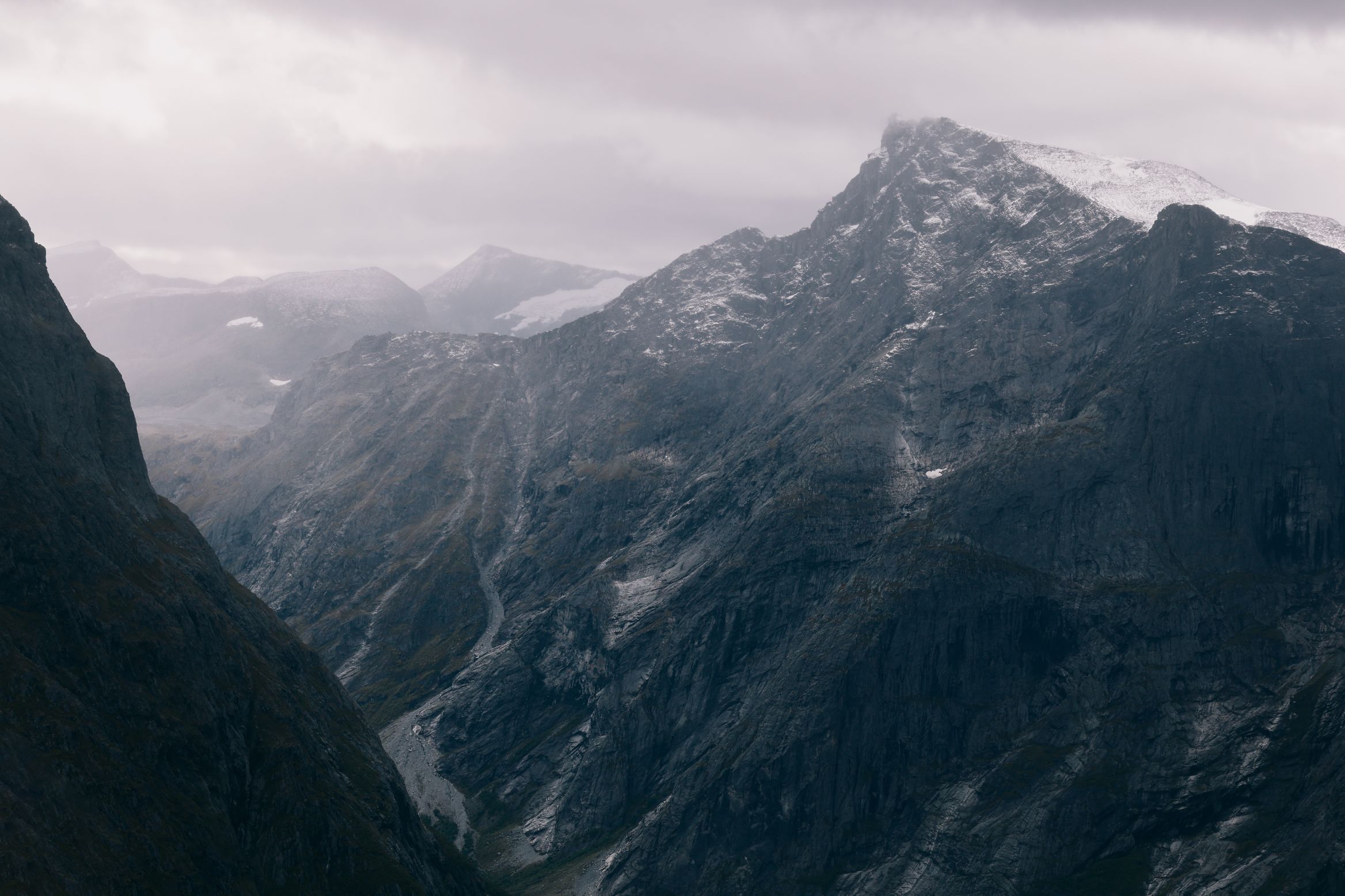Rain closing over a dark mountain face, the valley below lost in grey