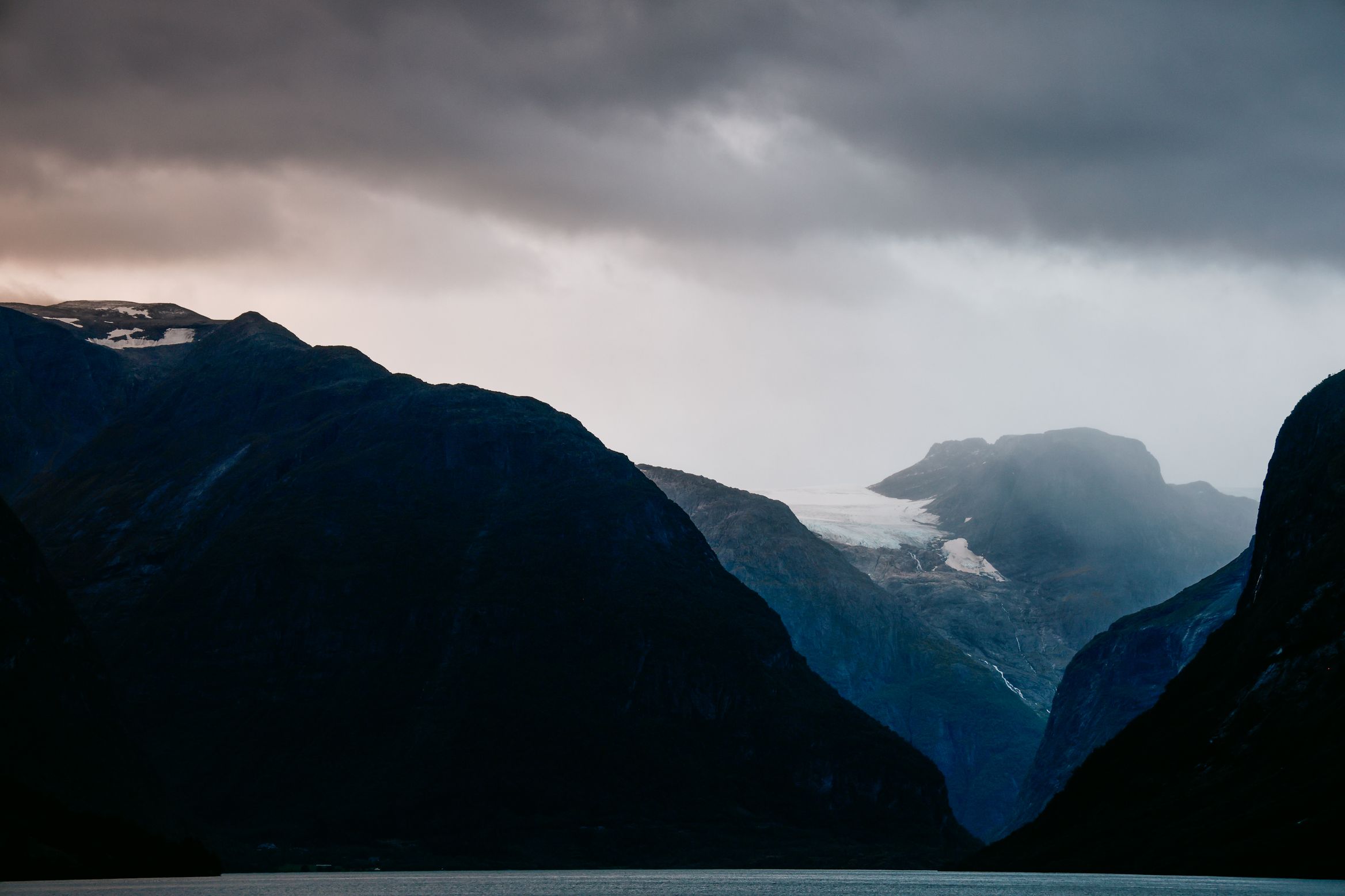 A glacier tongue glowing at the head of a fjord under thick evening cloud