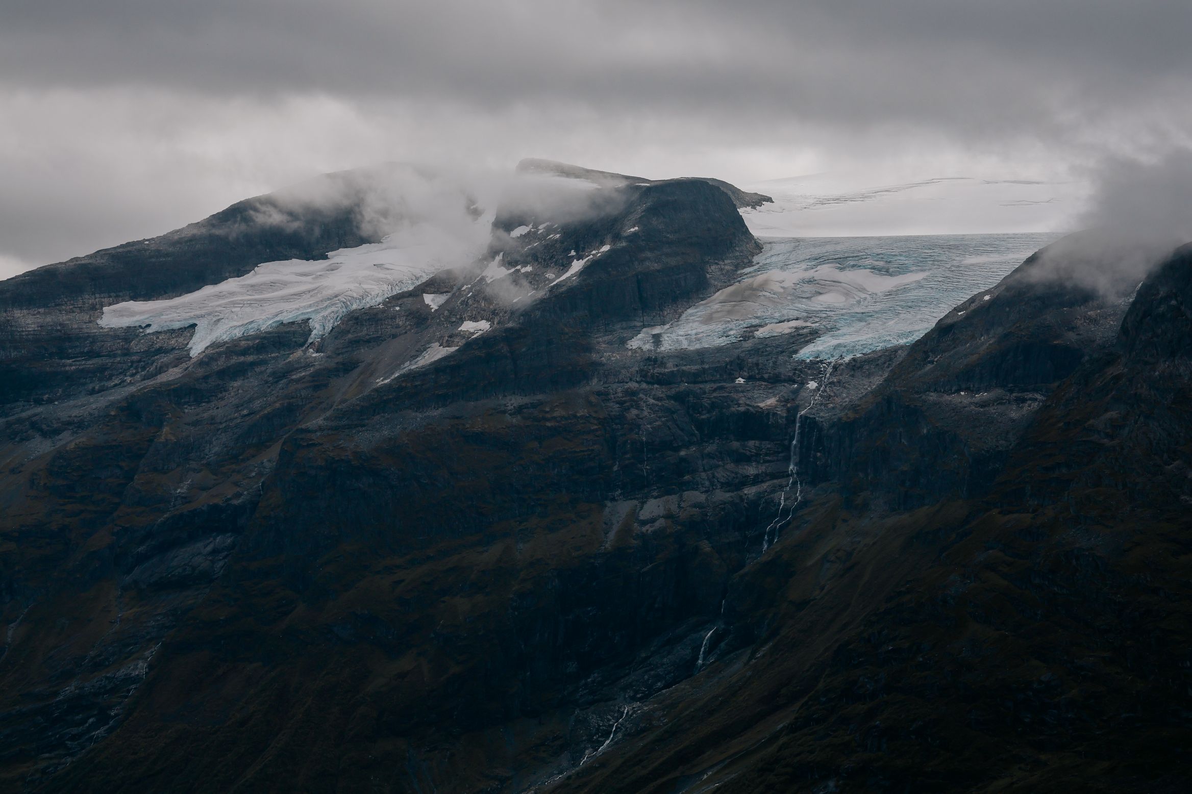 A blue glacier spilling over the lip of a plateau, cloud dragging across the ice