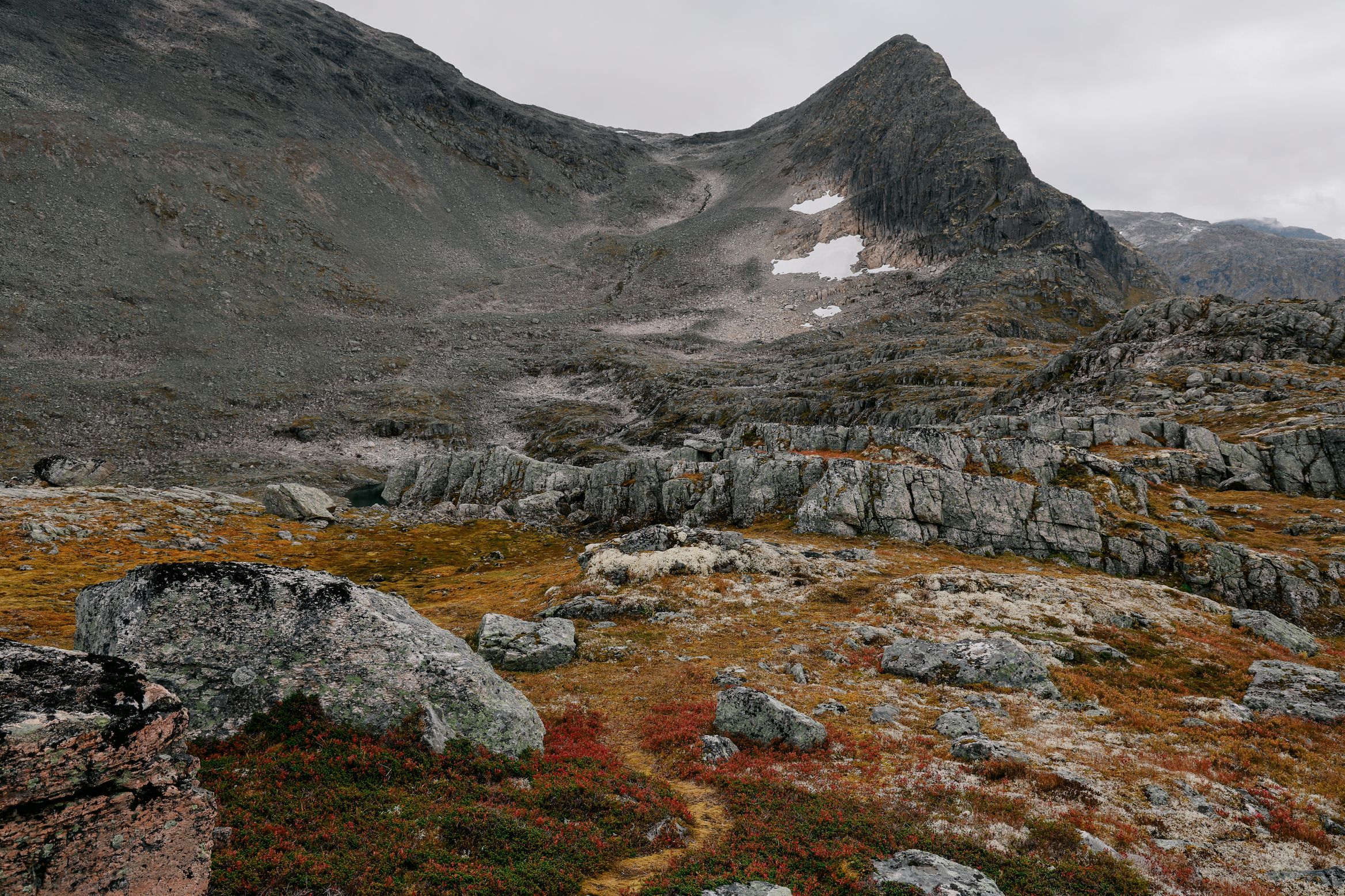 A pointed peak above a wide boulder plain, a single path winding through the autumn colour