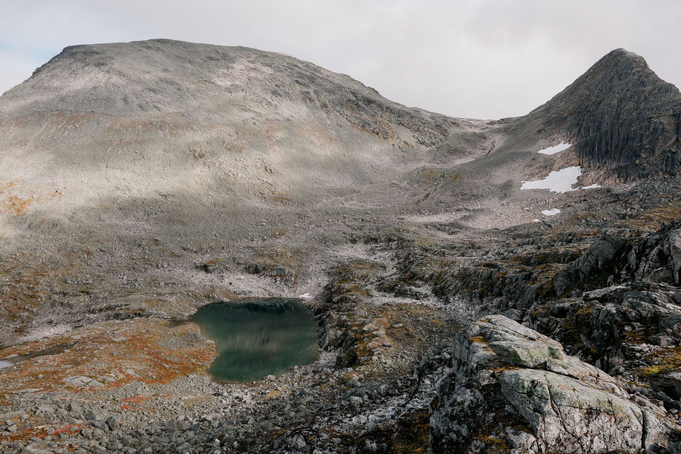 A green tarn held in a scoured granite basin below a bare dome of rock