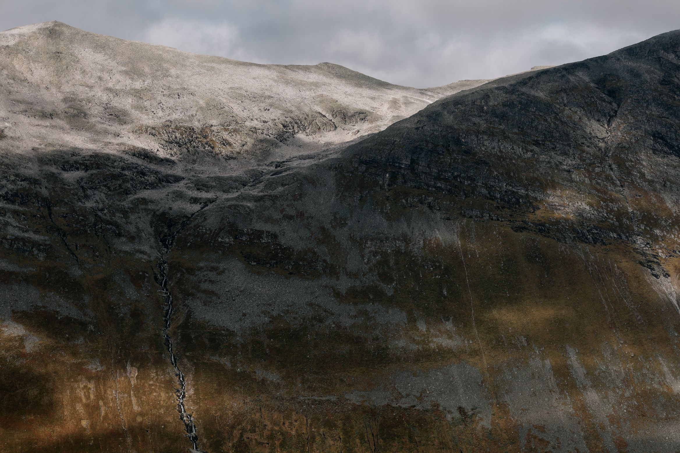 New snow lying over a broad hillside, the lower slopes still gold with grass