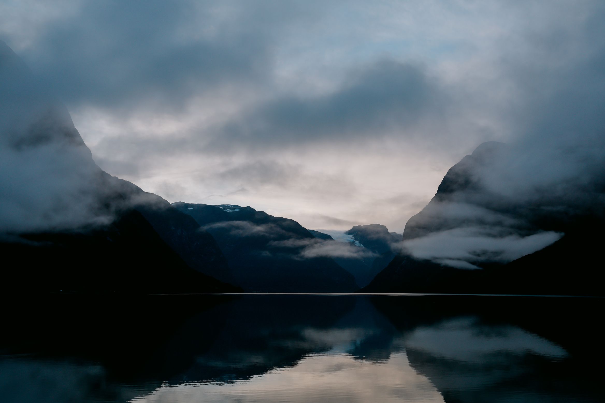 Dawn on a glassy fjord, cloud-wrapped mountains doubled in the reflection