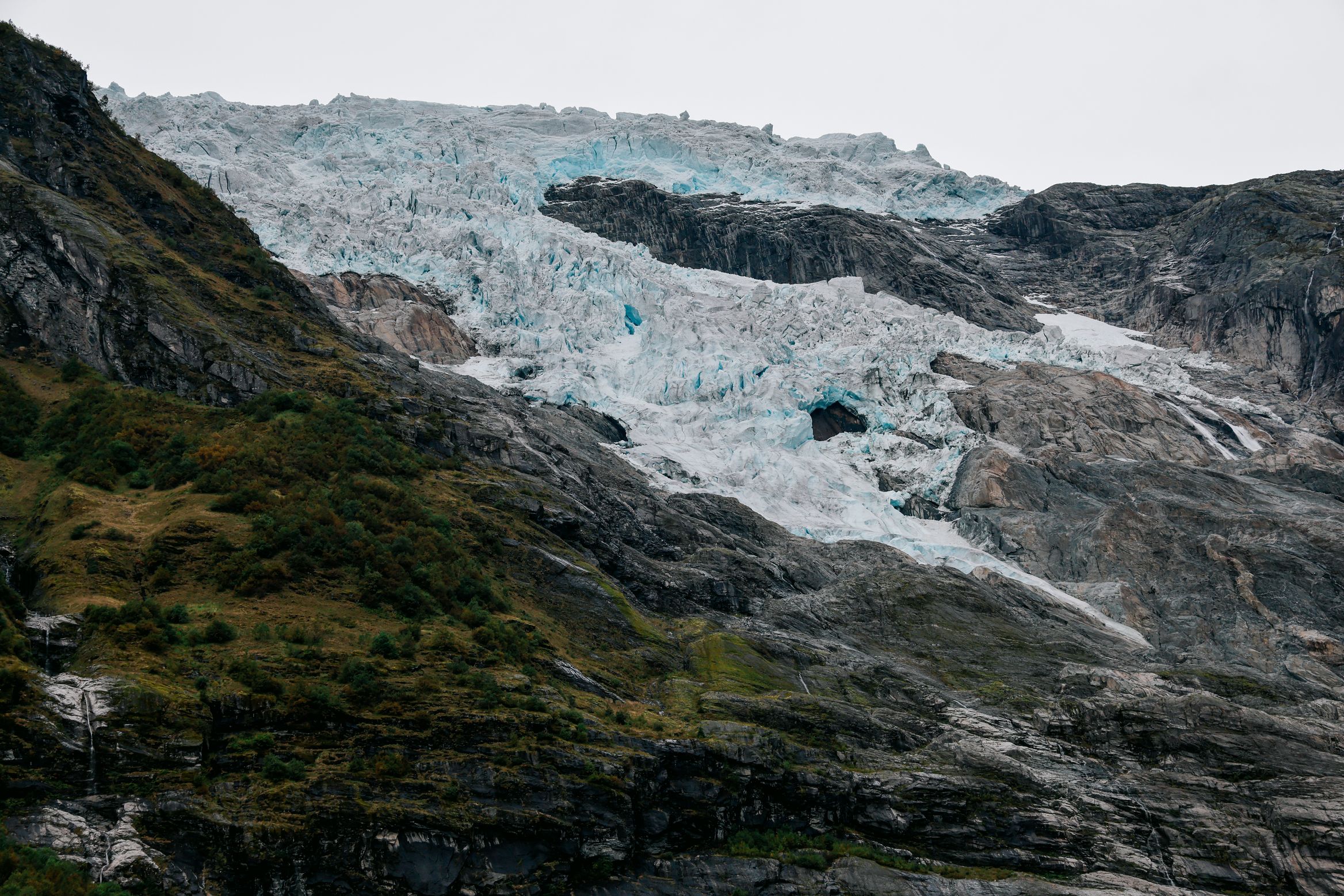 The blue broken ice of a glacier tongue hanging above bare rock slabs