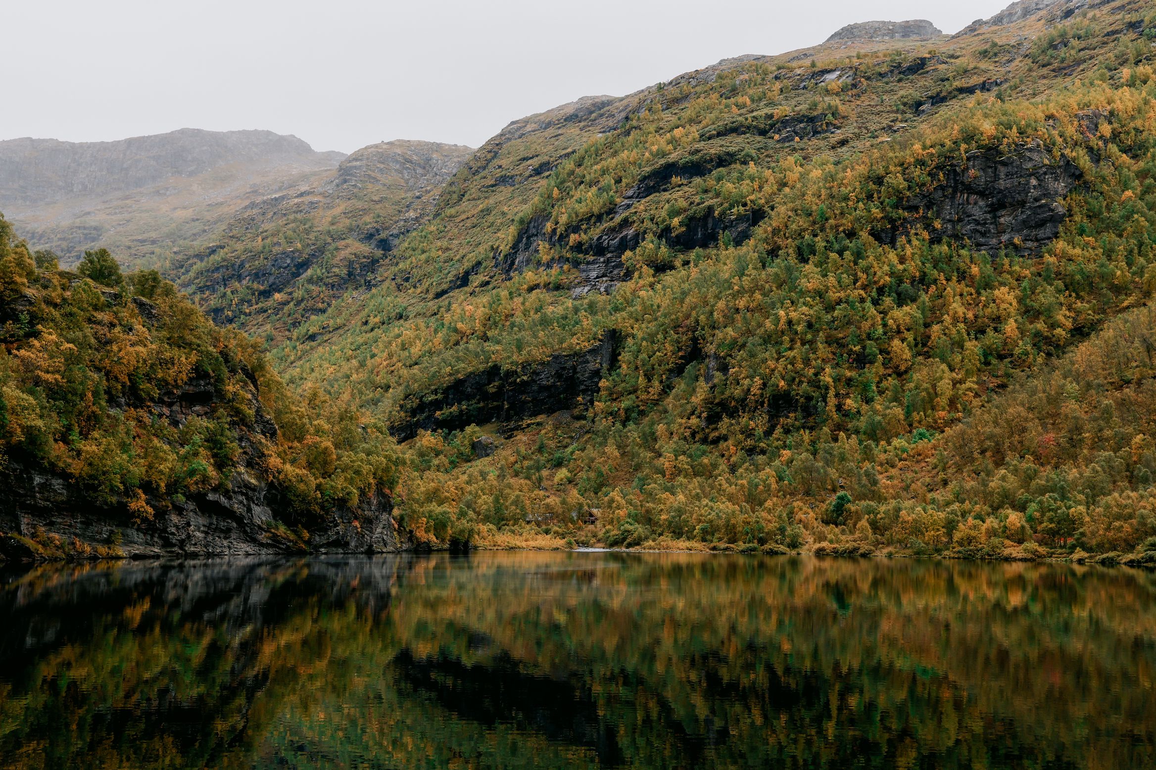 A still lake below wooded slopes, the birch woods just beginning to turn