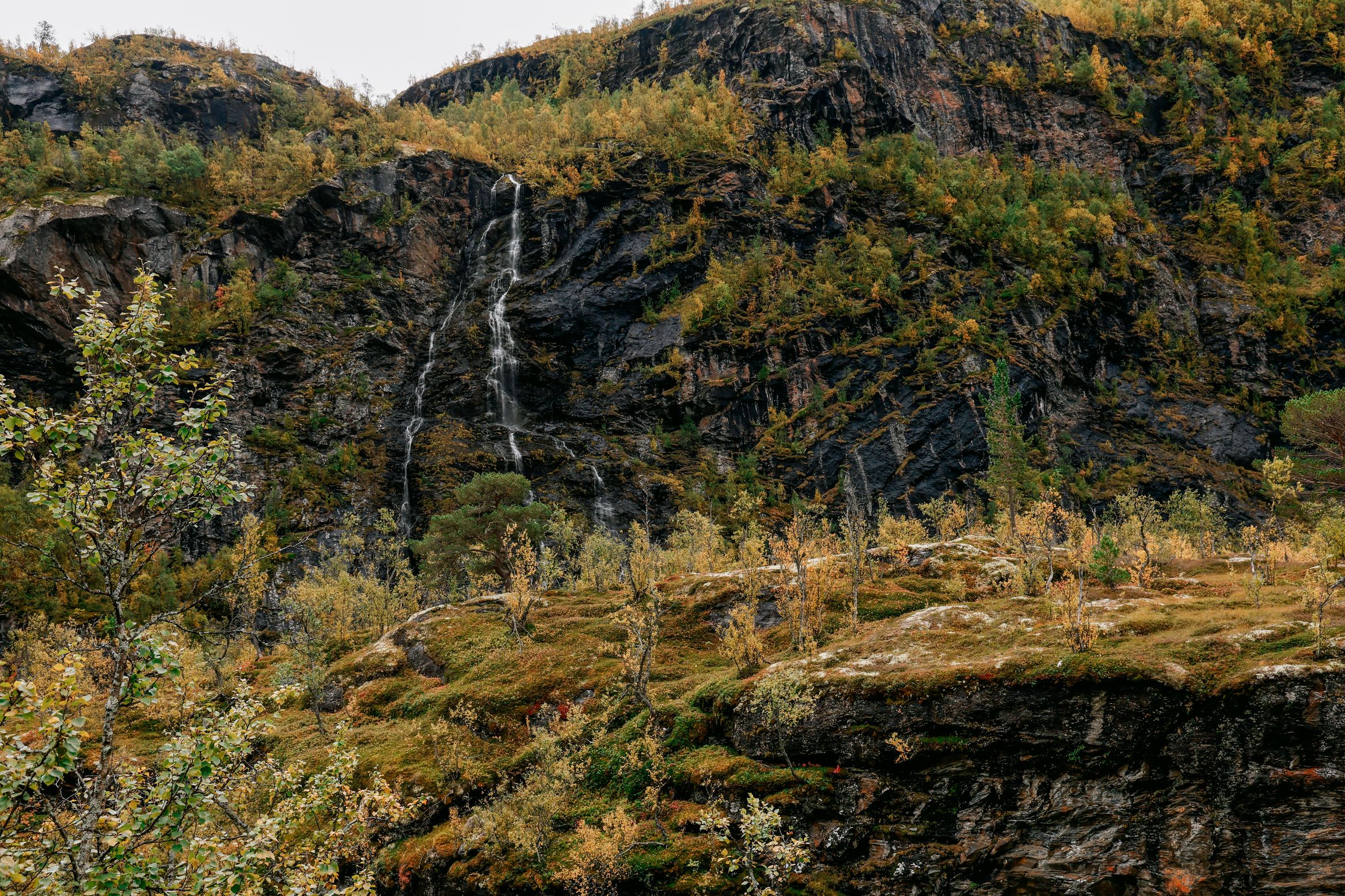 A waterfall threading down a wooded cliff face into the valley
