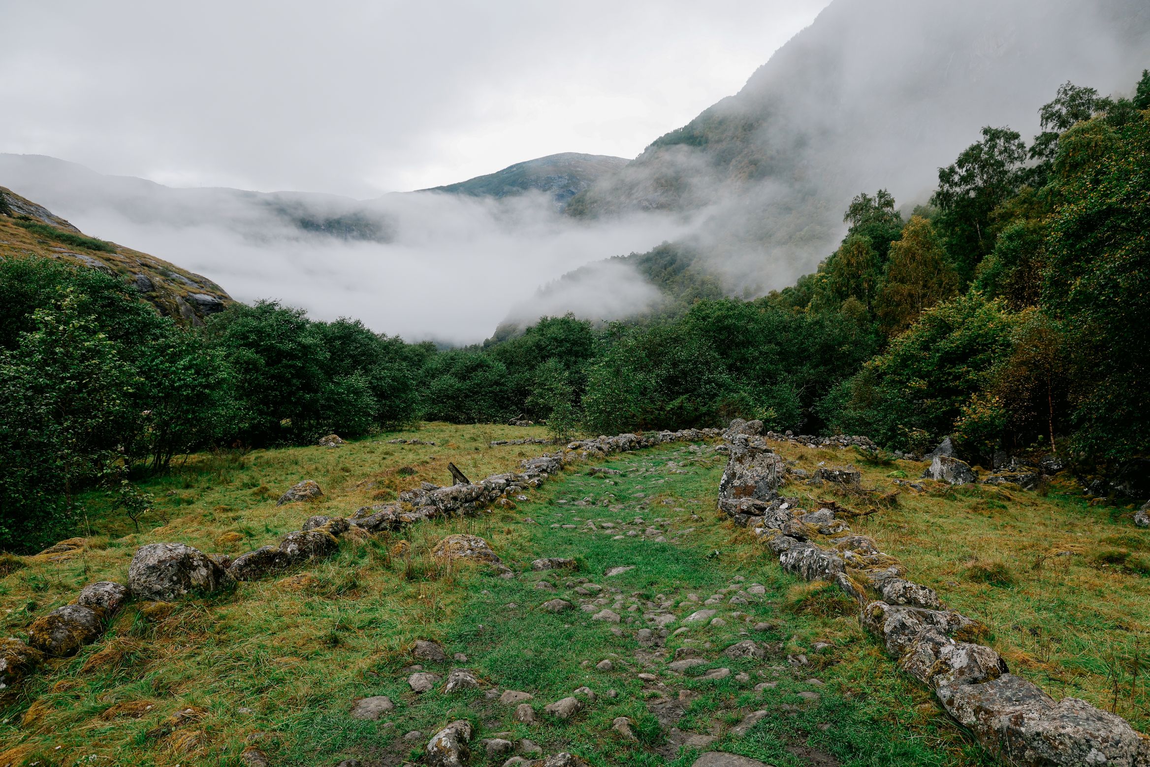 An old stone-walled drove road climbing into a valley filled with low cloud