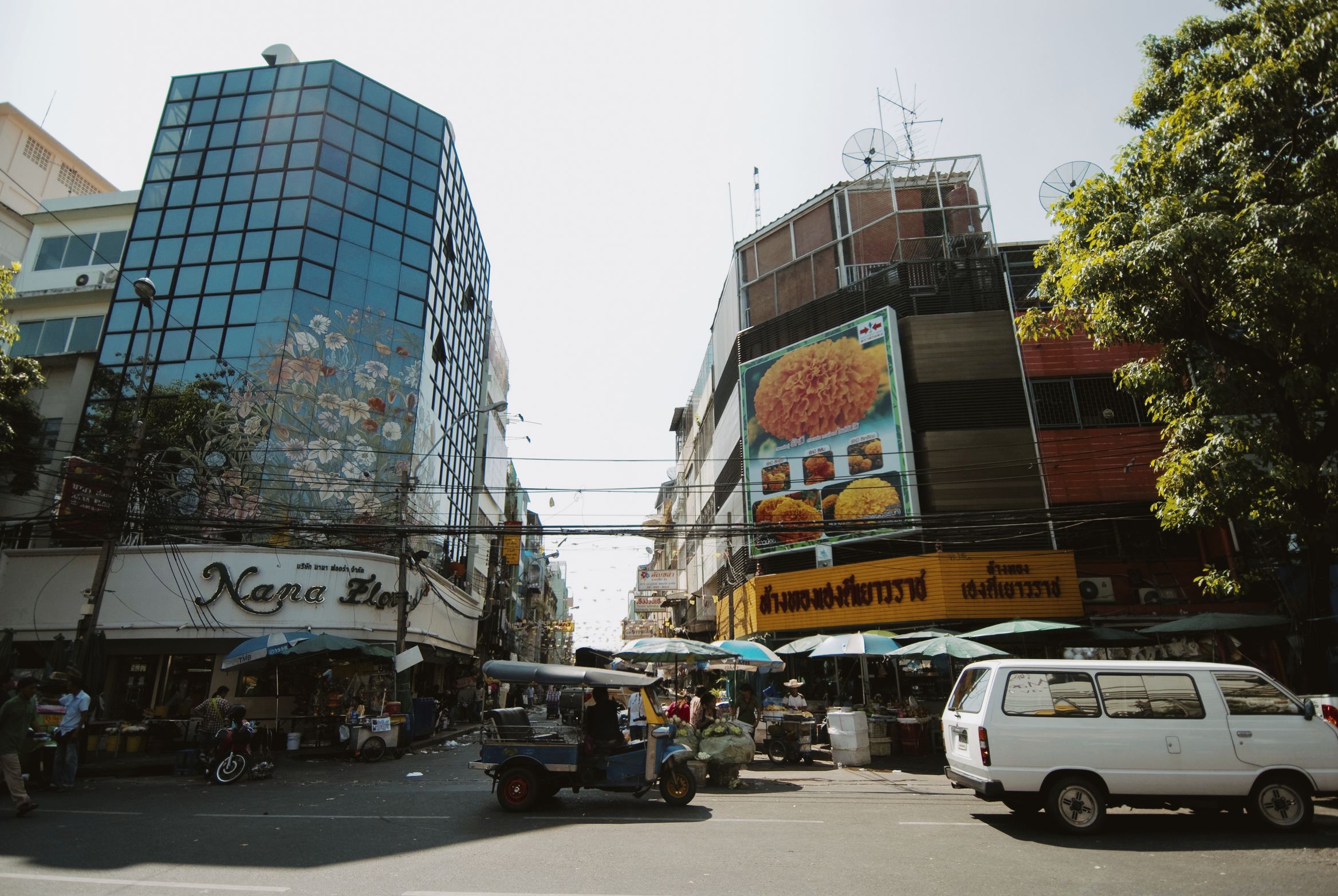 A street corner with a mirrored office block on one side and a tuk-tuk crossing the junction