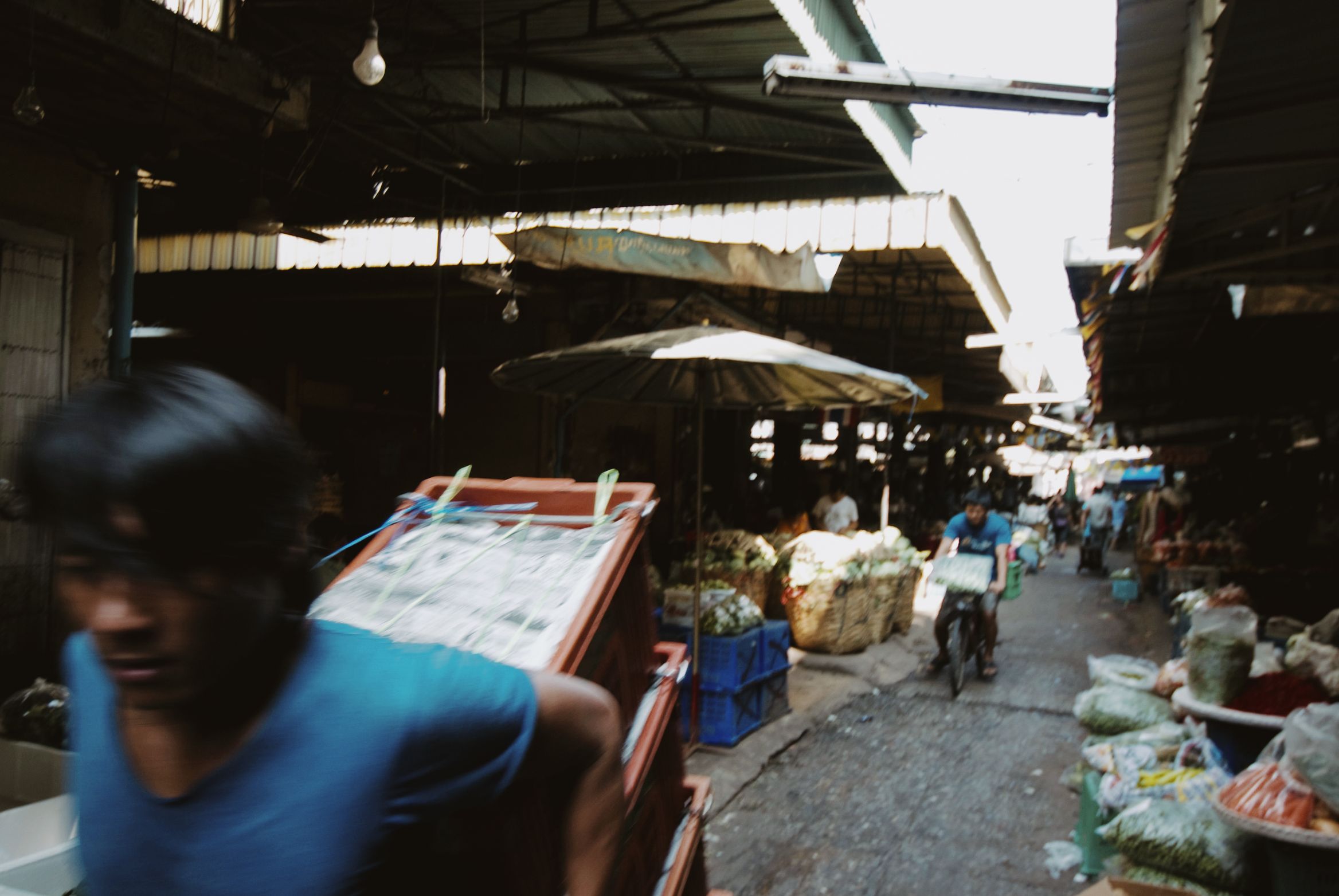 A man carrying a crate through a covered market, blurred as he passes the camera