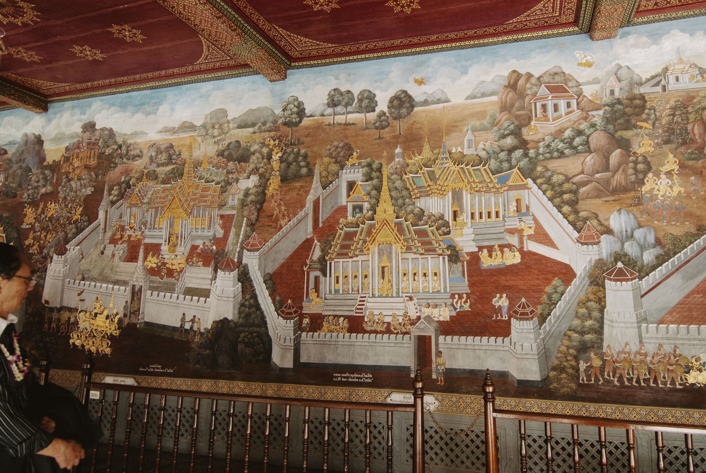 A visitor standing in front of a painted mural of a walled palace complex