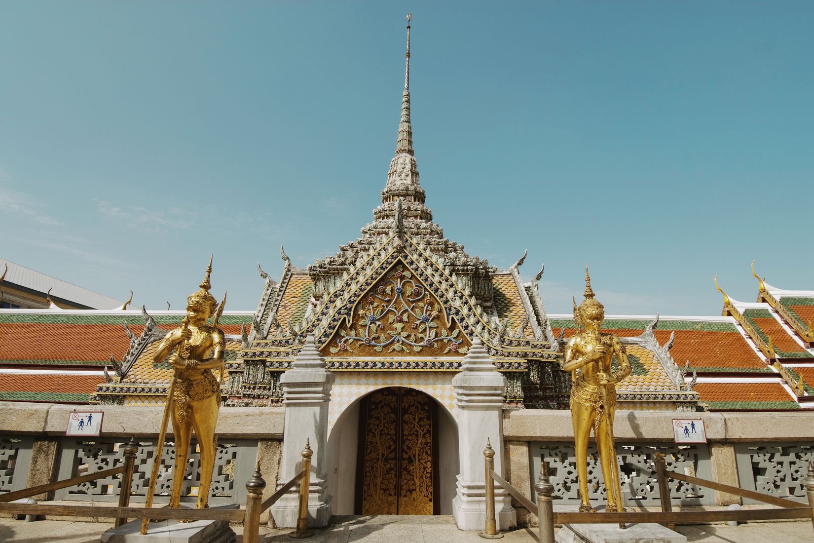 A tiled gateway with a gold kinnara standing either side of the steps