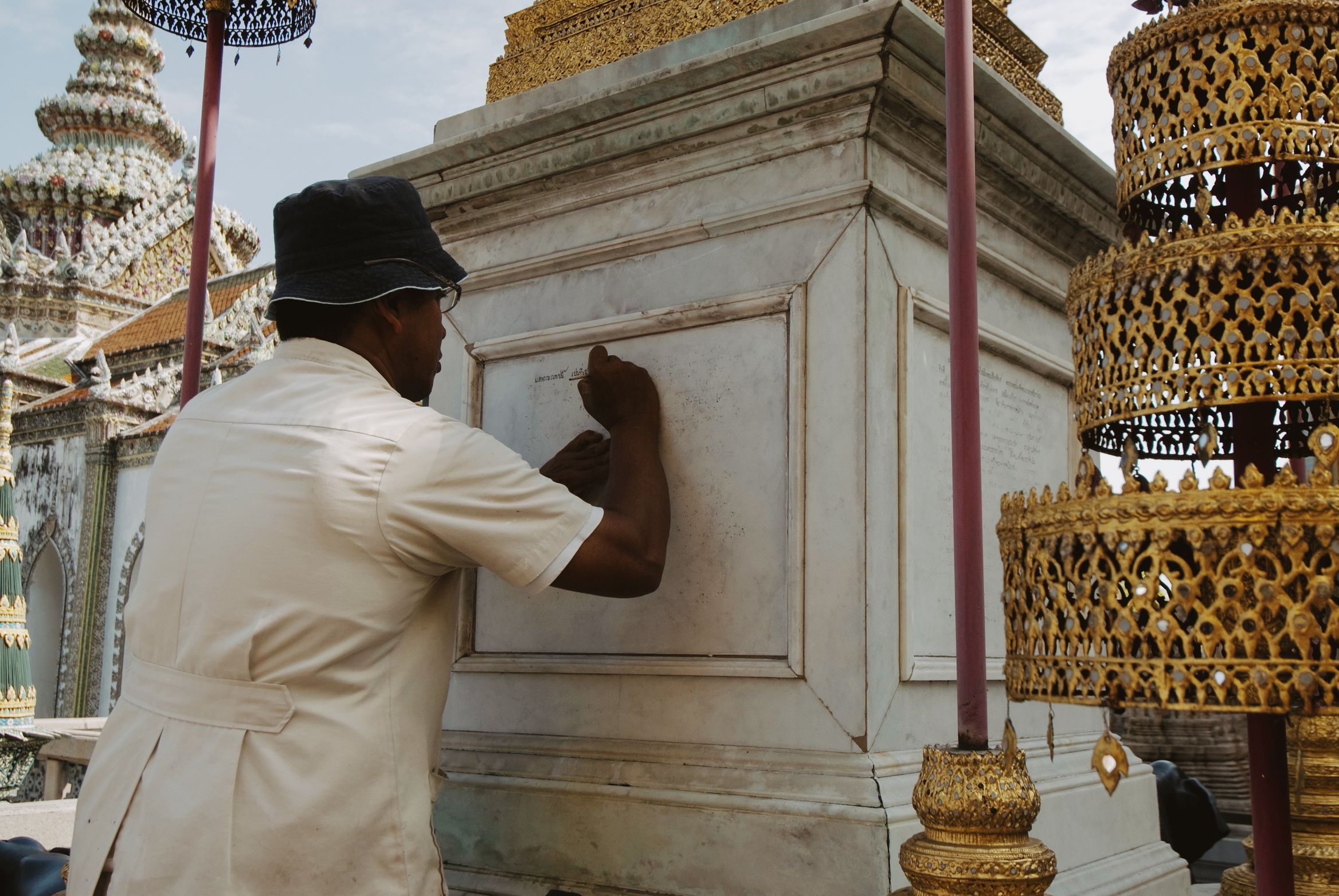 A man in a white uniform and sun hat cleaning the marble base of a shrine