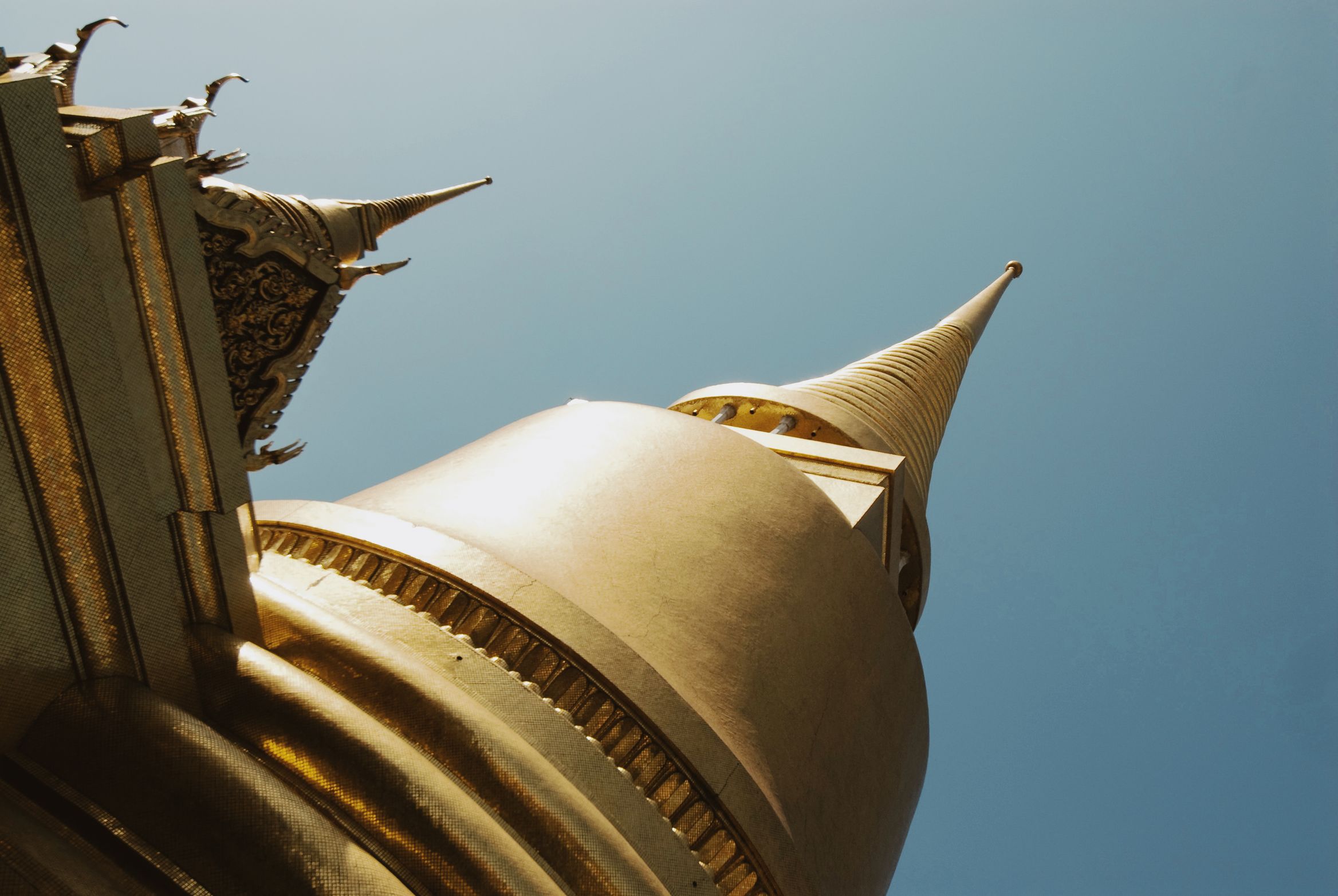 Looking straight up the side of a gold chedi to its spire against flat blue sky
