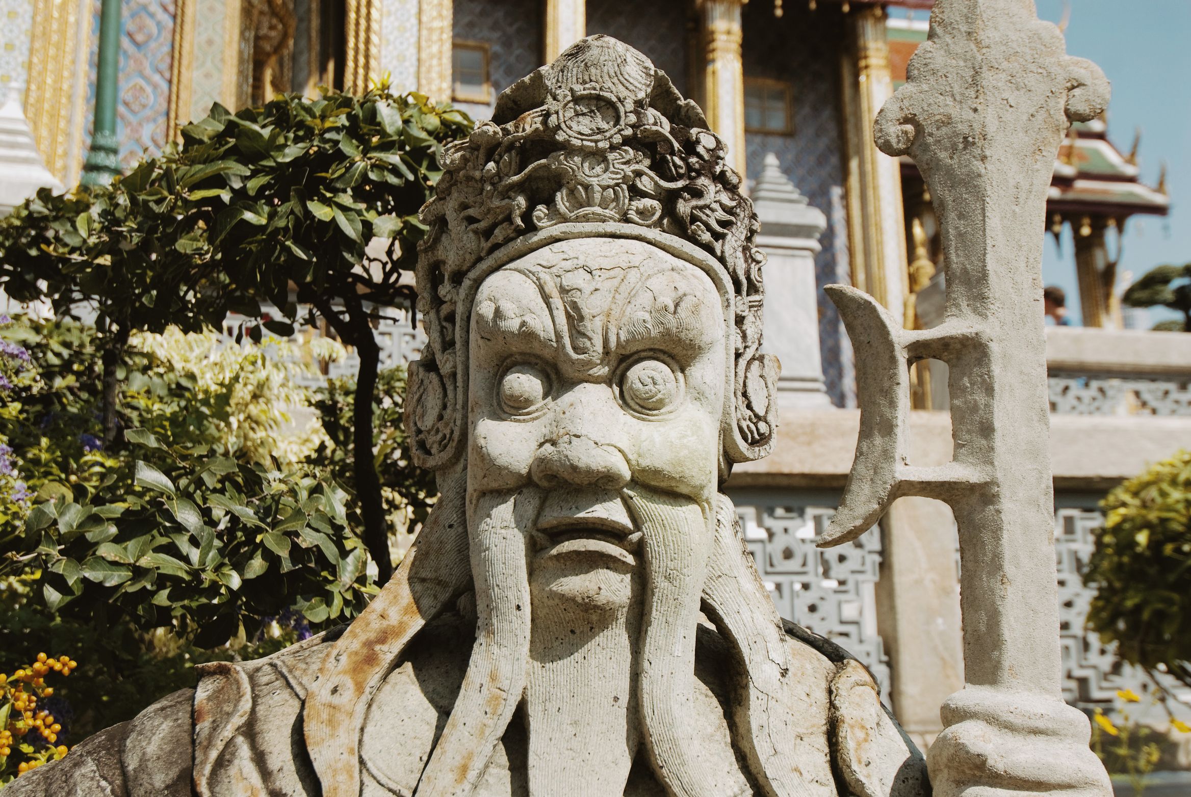 A Chinese stone guardian with a long beard and a halberd, standing under a tree