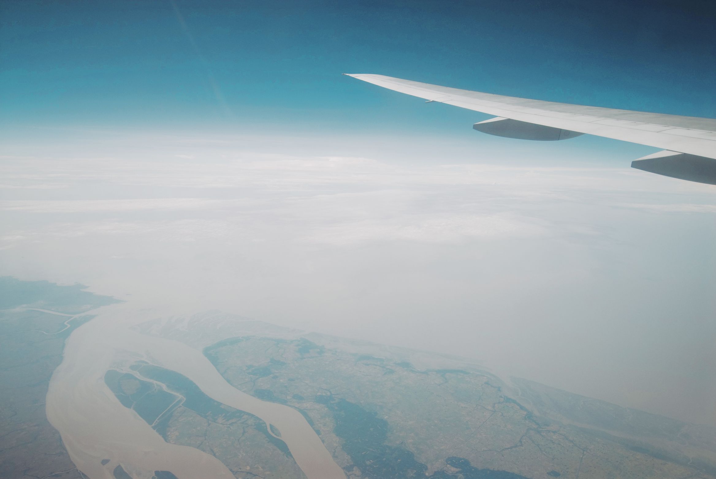A brown river winding through haze far below the wing, sky deepening above