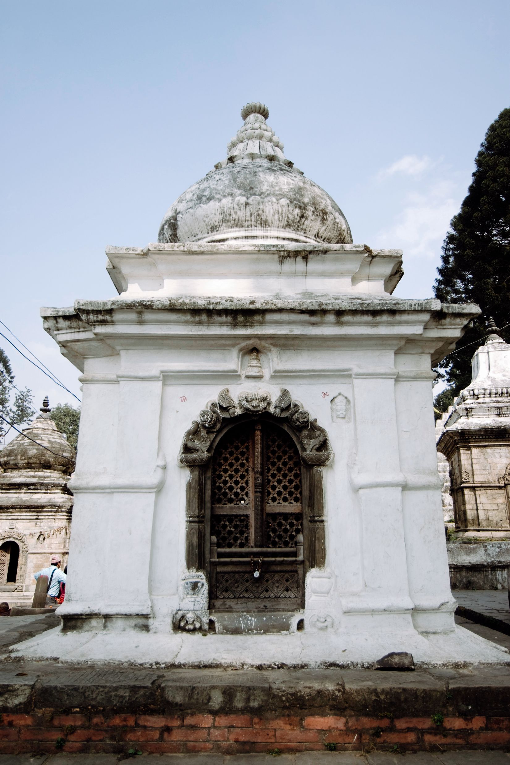 A whitewashed votive shrine with a lattice door and a weathered dome, against a pale sky