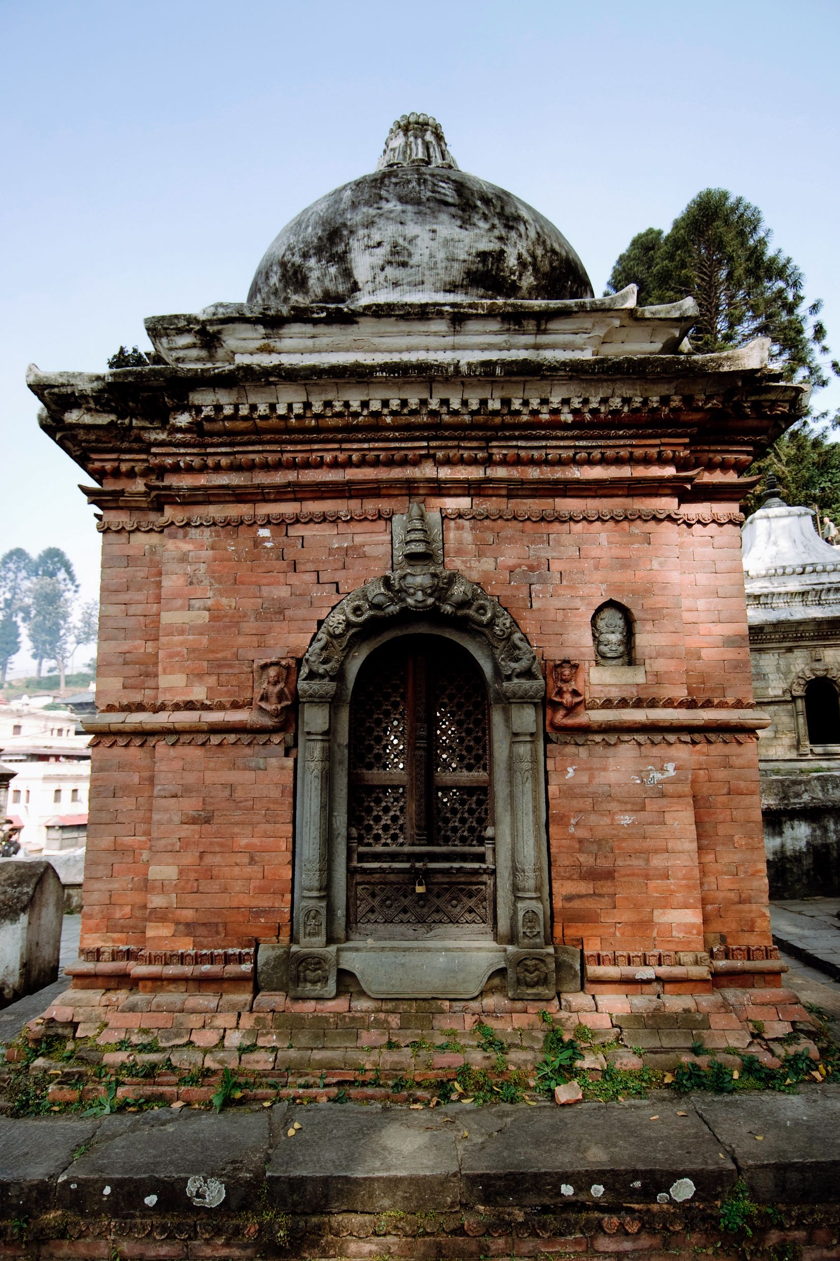 A brick shrine with a carved stone doorframe and a soot-dark dome, the valley dropping away behind